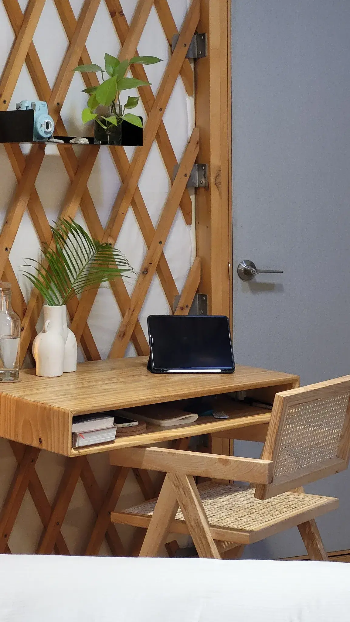 Minimalist yurt workspace with a wooden desk, woven chair, indoor plants, and a cozy, sustainable design.