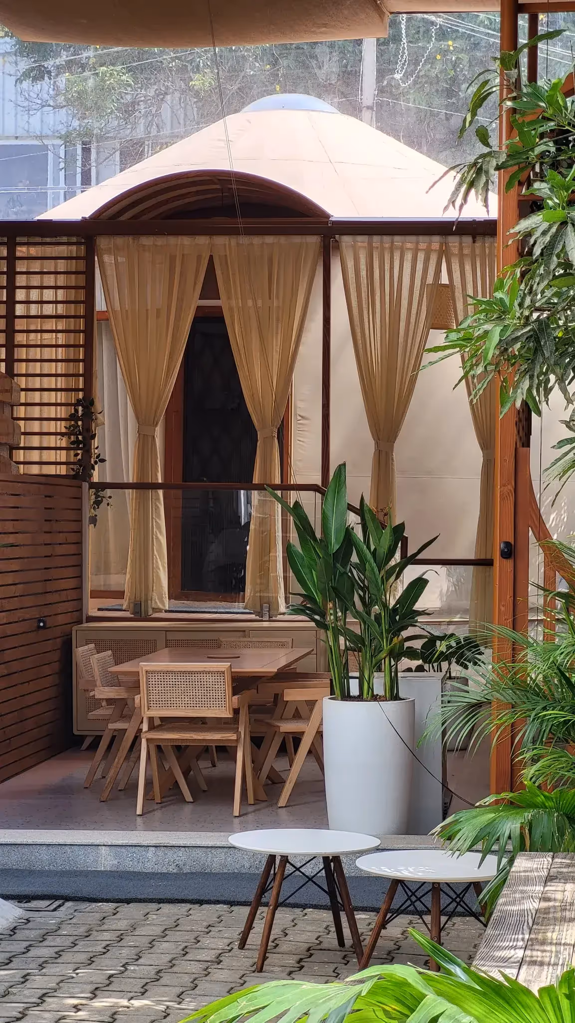 Luxury yurt entrance with sheer curtains, wooden furniture, and lush greenery, creating a tranquil outdoor retreat.