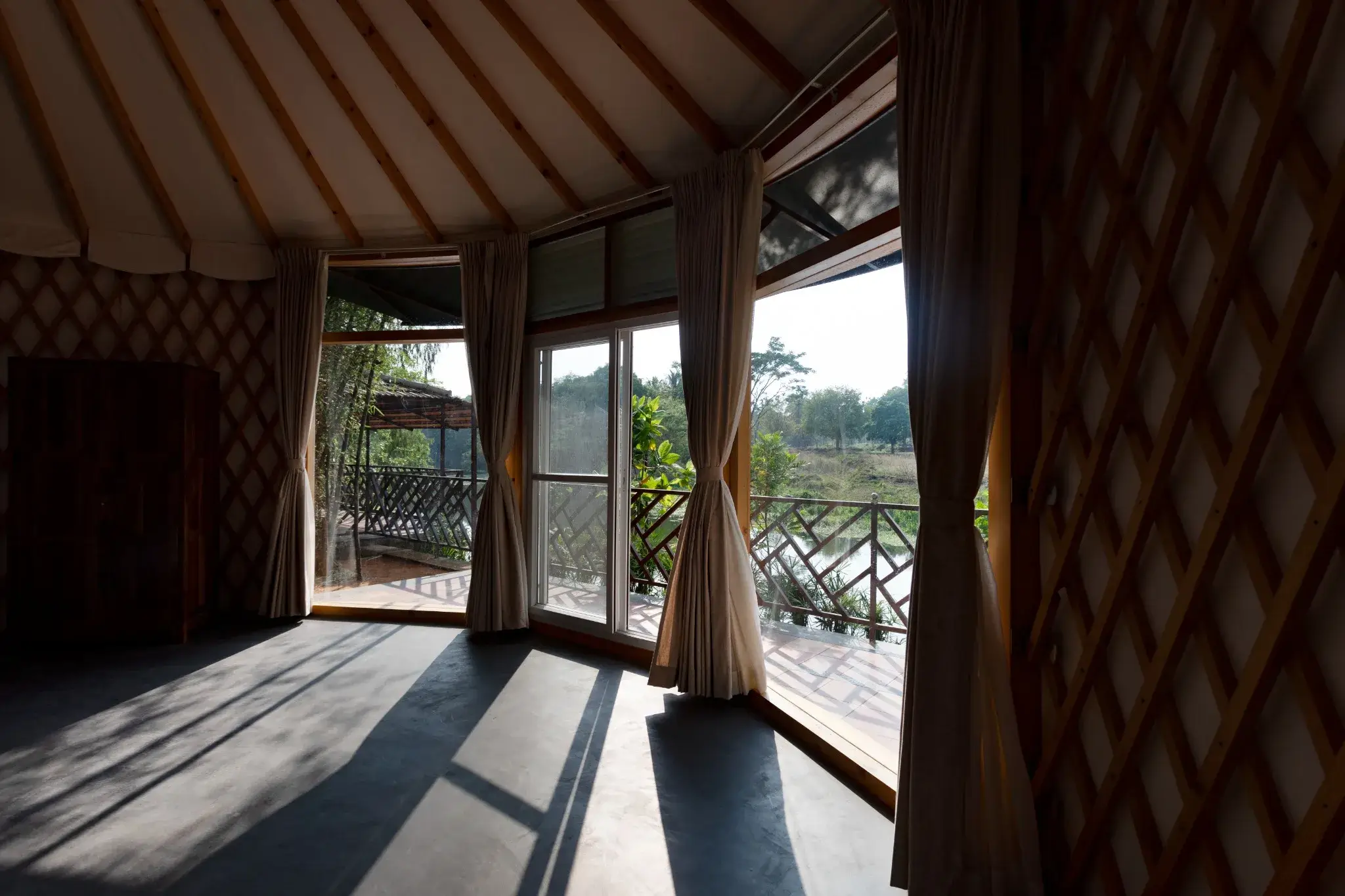Yurts interior with panoramic windows, curtains, lattice walls, and deck overlooking trees, railing, and river
