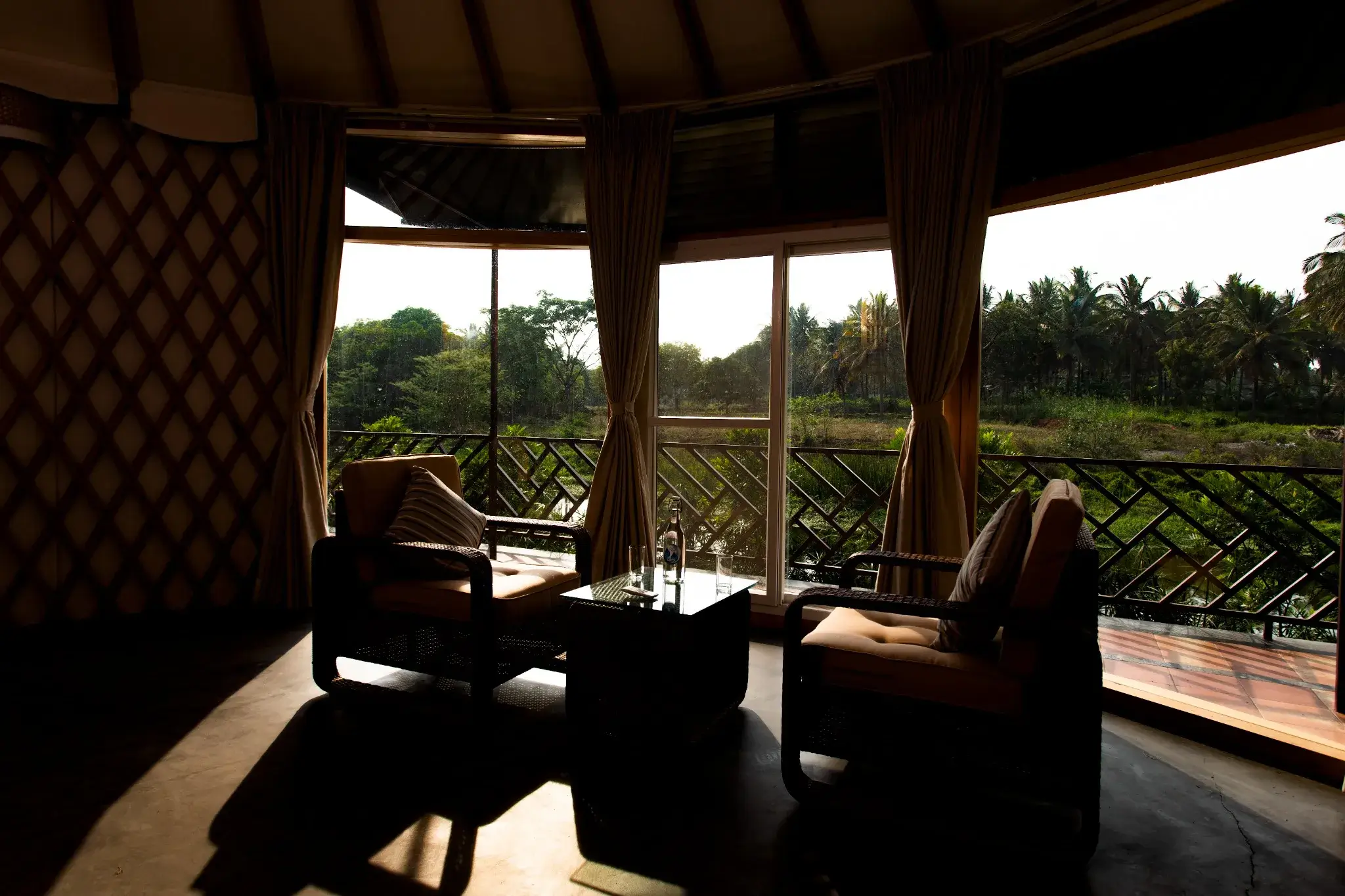 Luxury yurt interior with two lounge chairs, glass wall, and view of tropical greenery and palm trees
