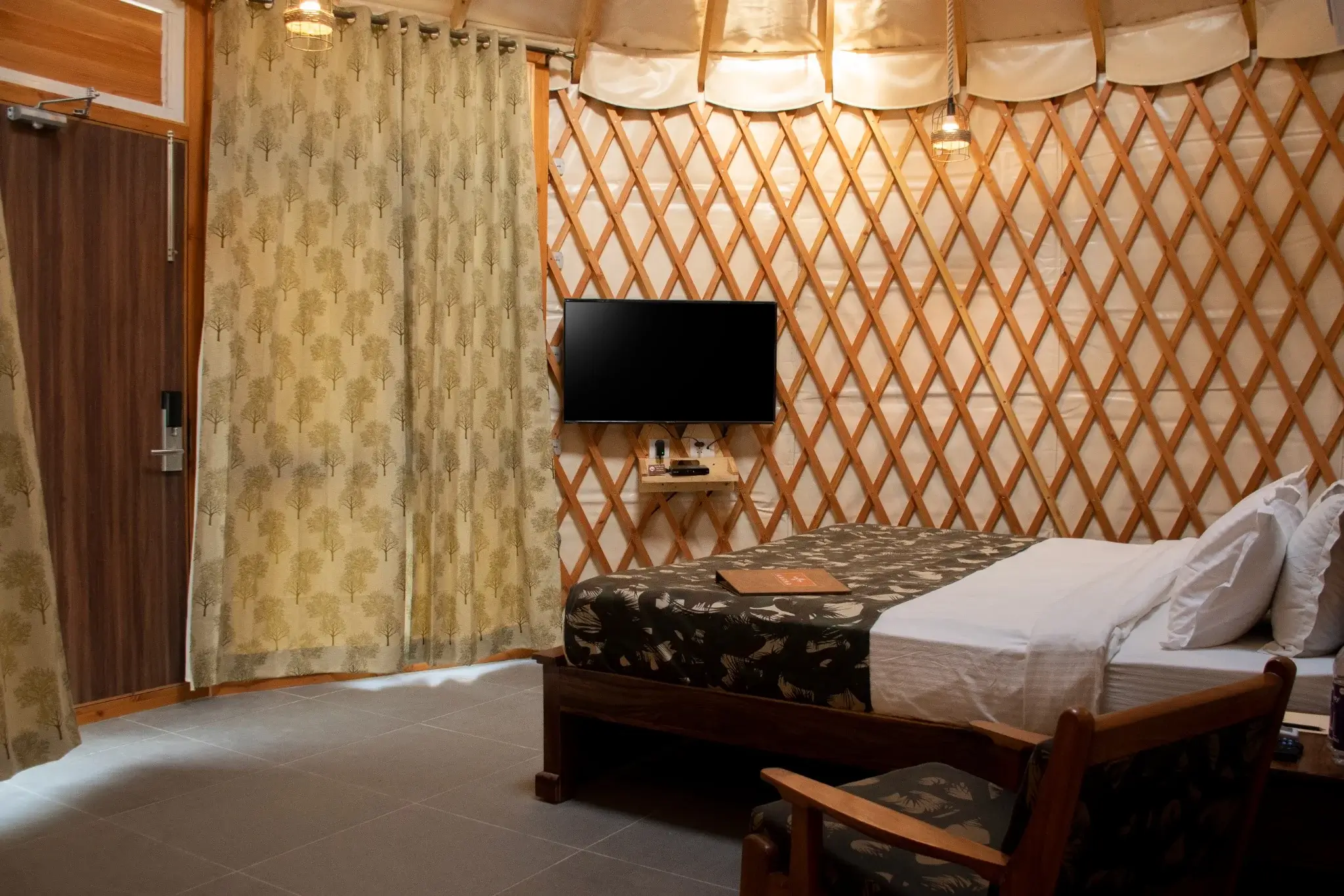 Cozy yurts bedroom interior featuring lattice walls, double bed, wall-mounted TV, curtains, and pendant lights
