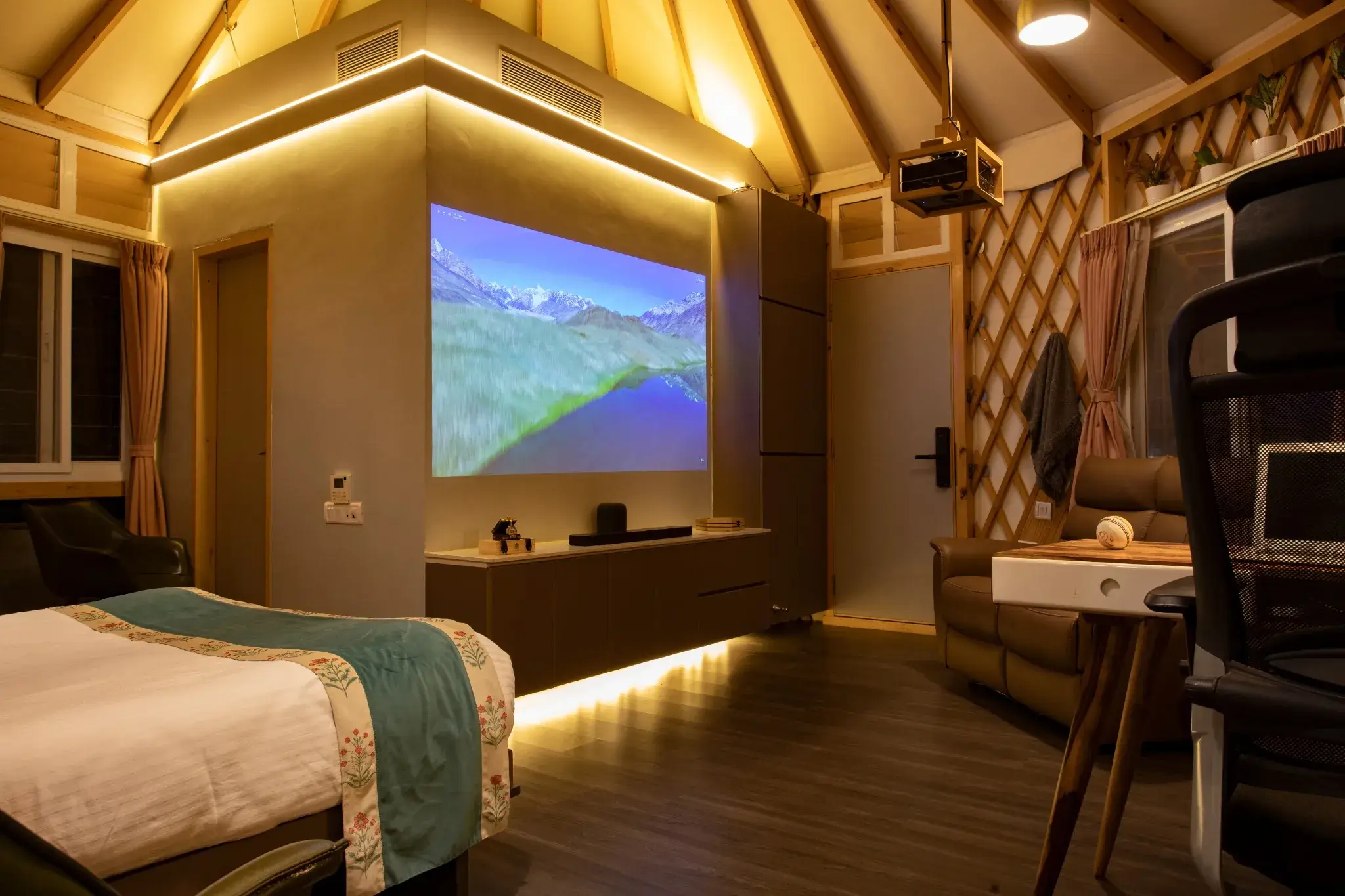 Contemporary yurts interior featuring projector screen, warm lighting, bed, leather sofa, lattice walls, and wooden beams