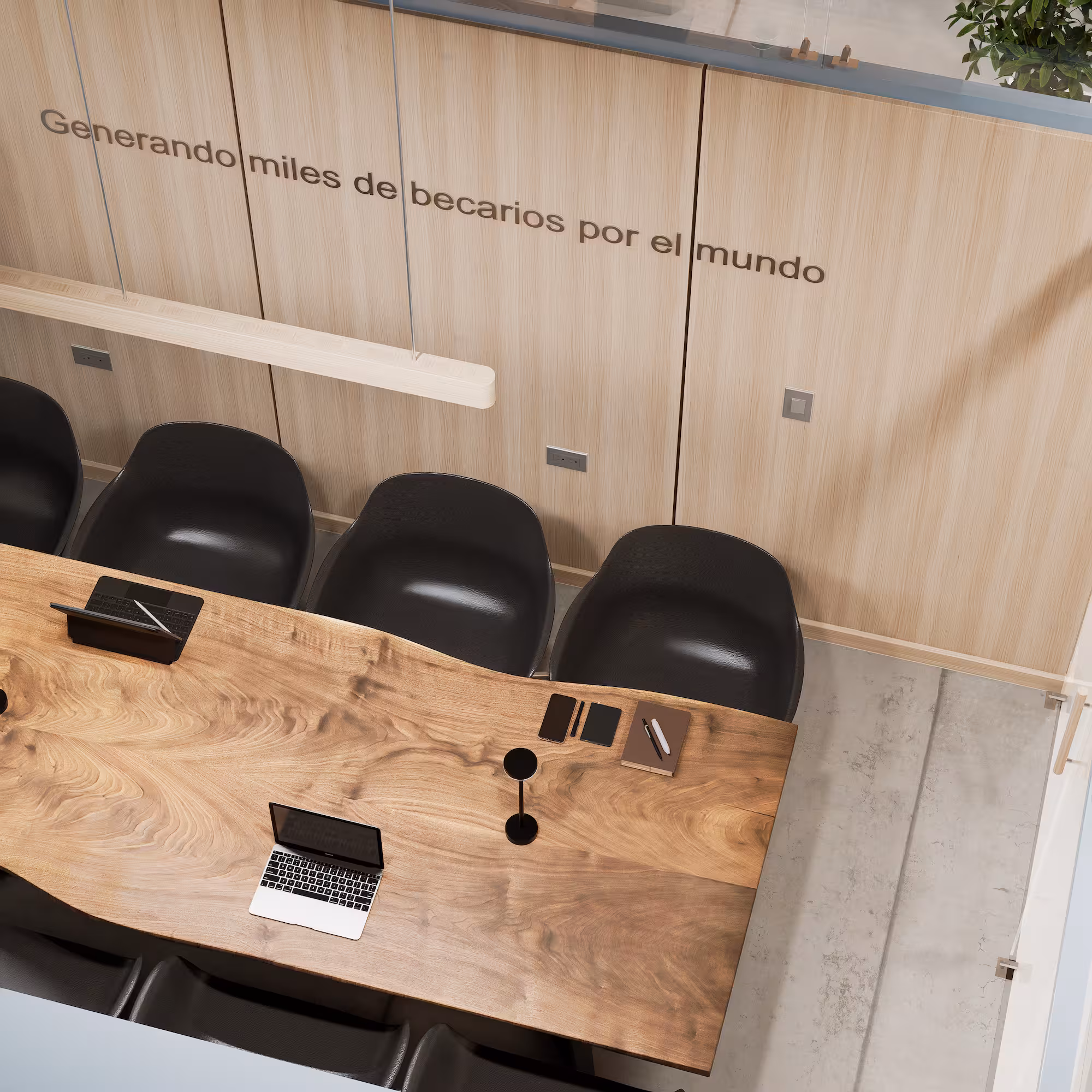 Mesa de reunión de madera con laptops, cuadernos y sillas negras junto a pared con texto en español.
