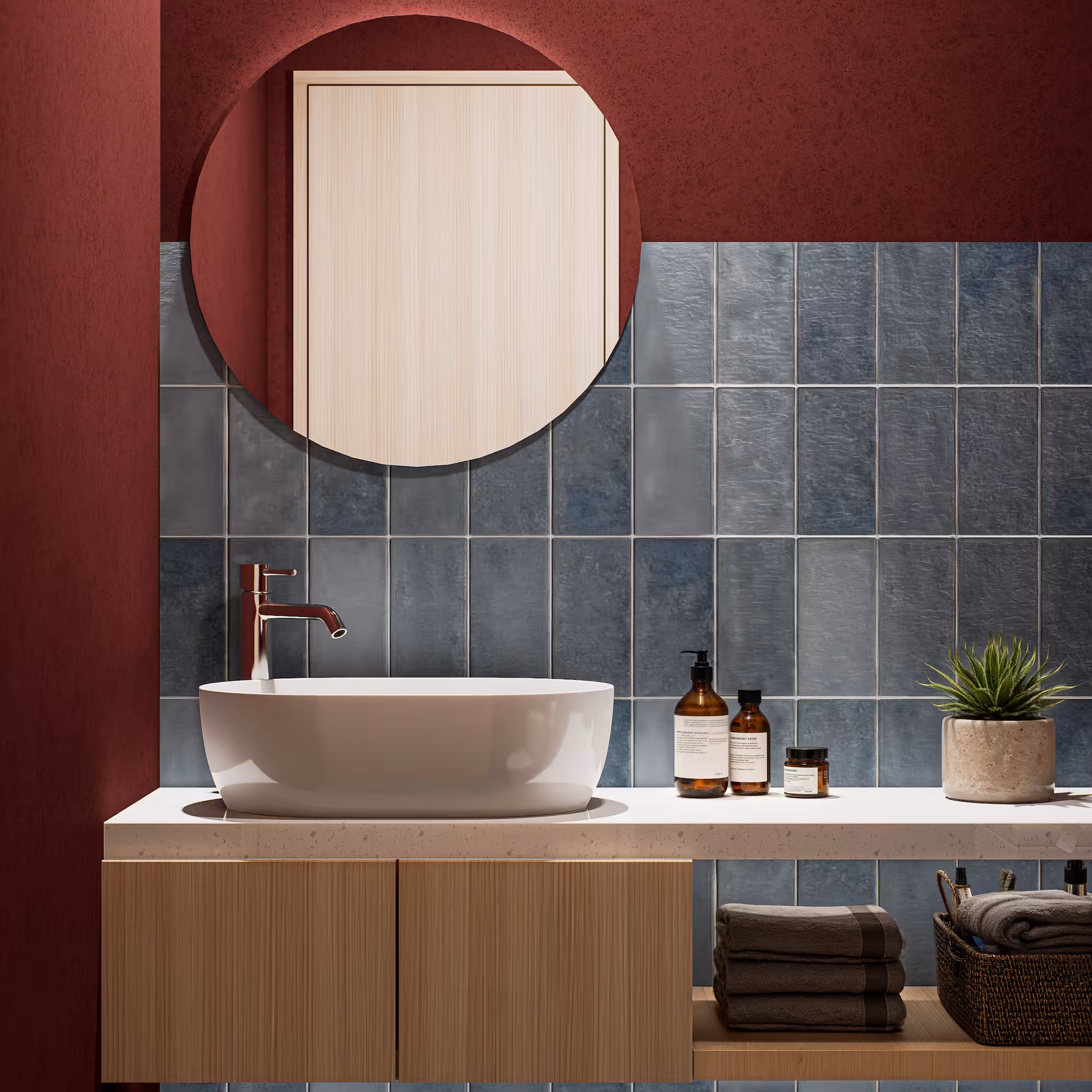 Lavabo blanco sobre encimera con espejo redondo, toallas y planta en baño con azulejos azules.