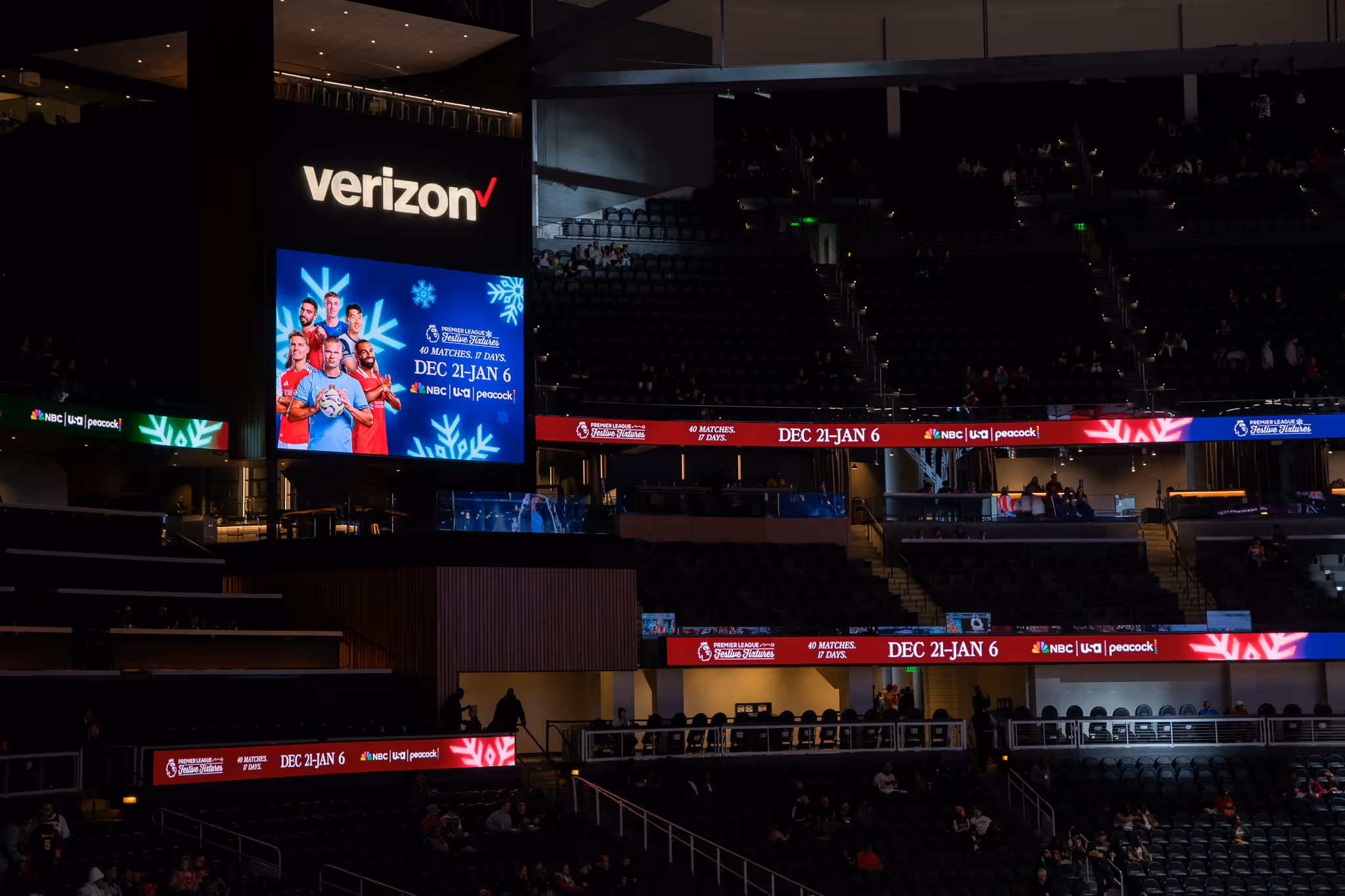 Indoor stadium with Verizon logo and digital screens advertising Premier League Festive Fixtures from Dec 21 to Jan 6.