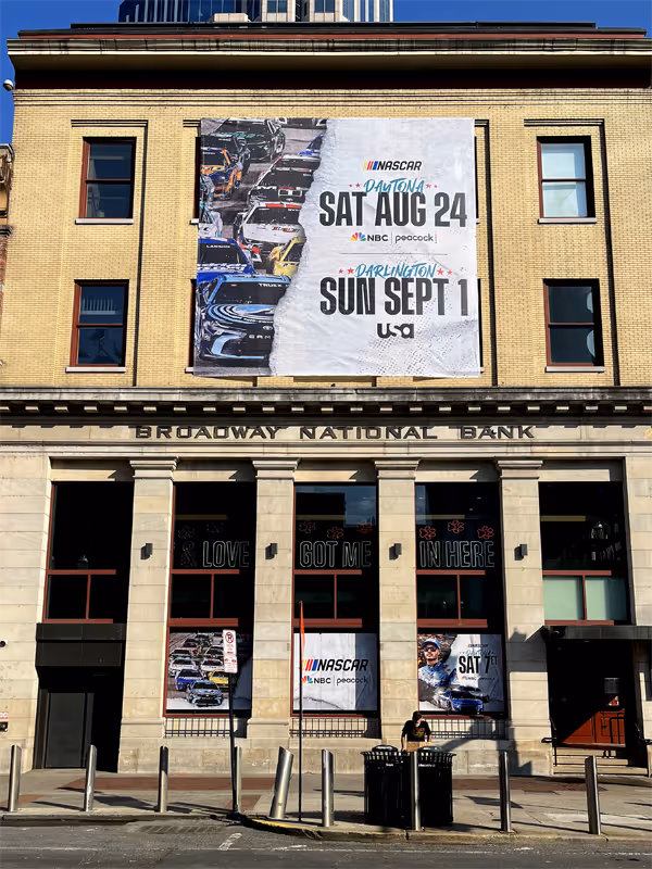 Historic Broadway National Bank building with large NASCAR banners promoting races on August 24 at Daytona and September 1 at Darlington.