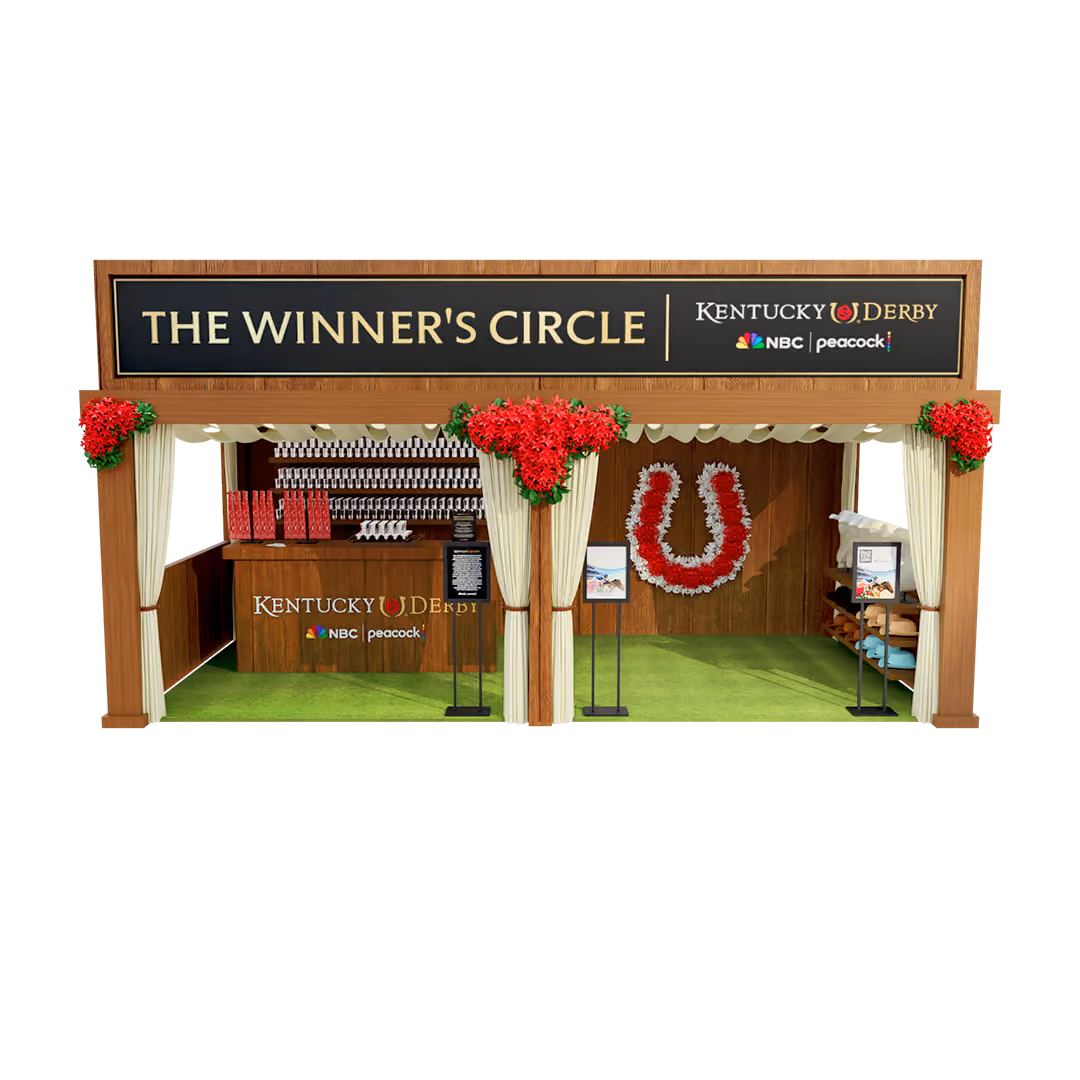 A decorated wooden booth labeled 'THE WINNER'S CIRCLE' for the Kentucky Derby, featuring red floral arrangements, a garland shaped like a horseshoe, a counter with Kentucky Derby branding, and logos for NBC and Peacock.