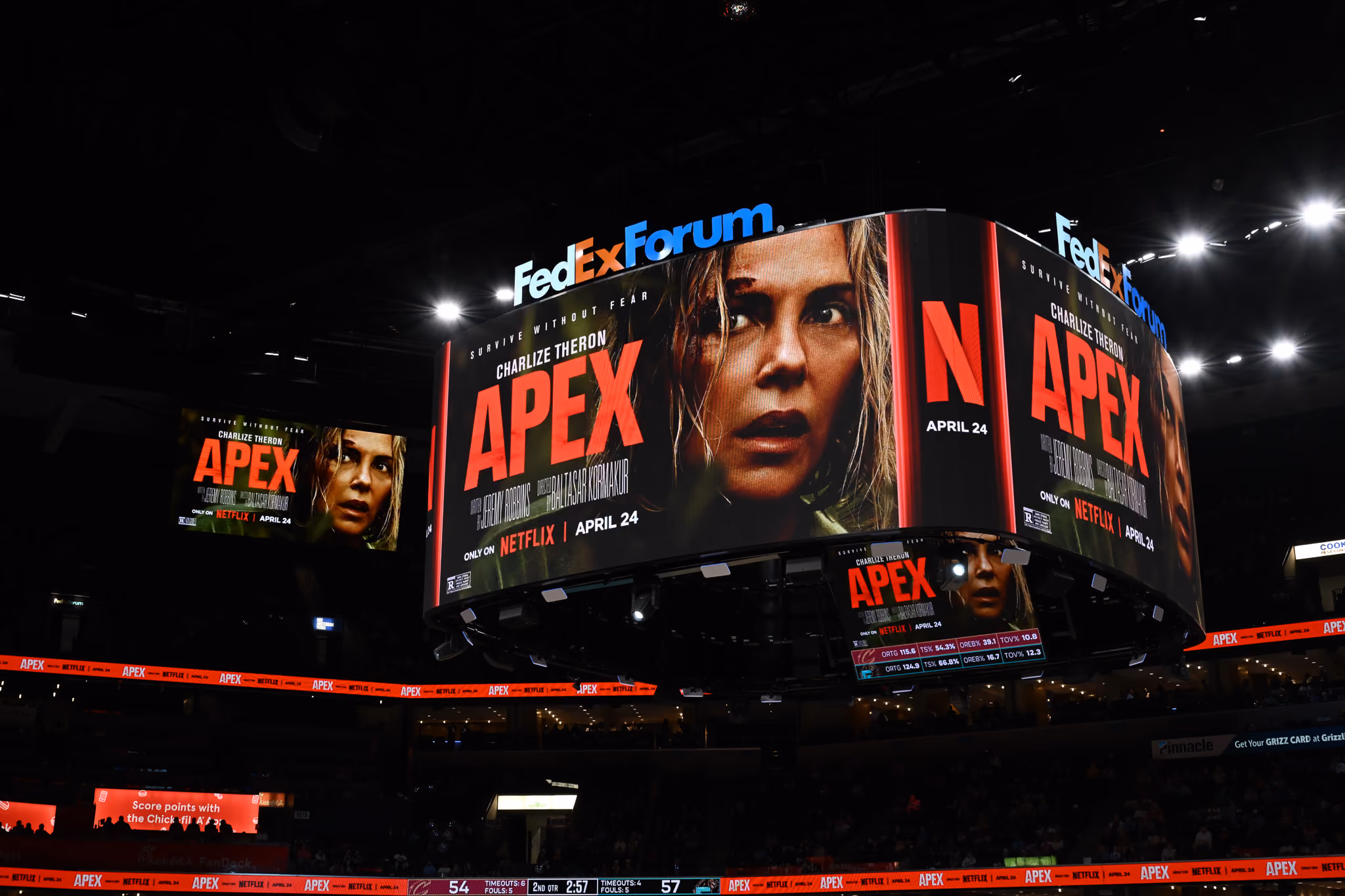 Large arena scoreboard at FedExForum displaying a promotional advertisement for the Netflix movie 'Apex' starring Charlize Theron, with her face prominently shown and an April 24 release date.
