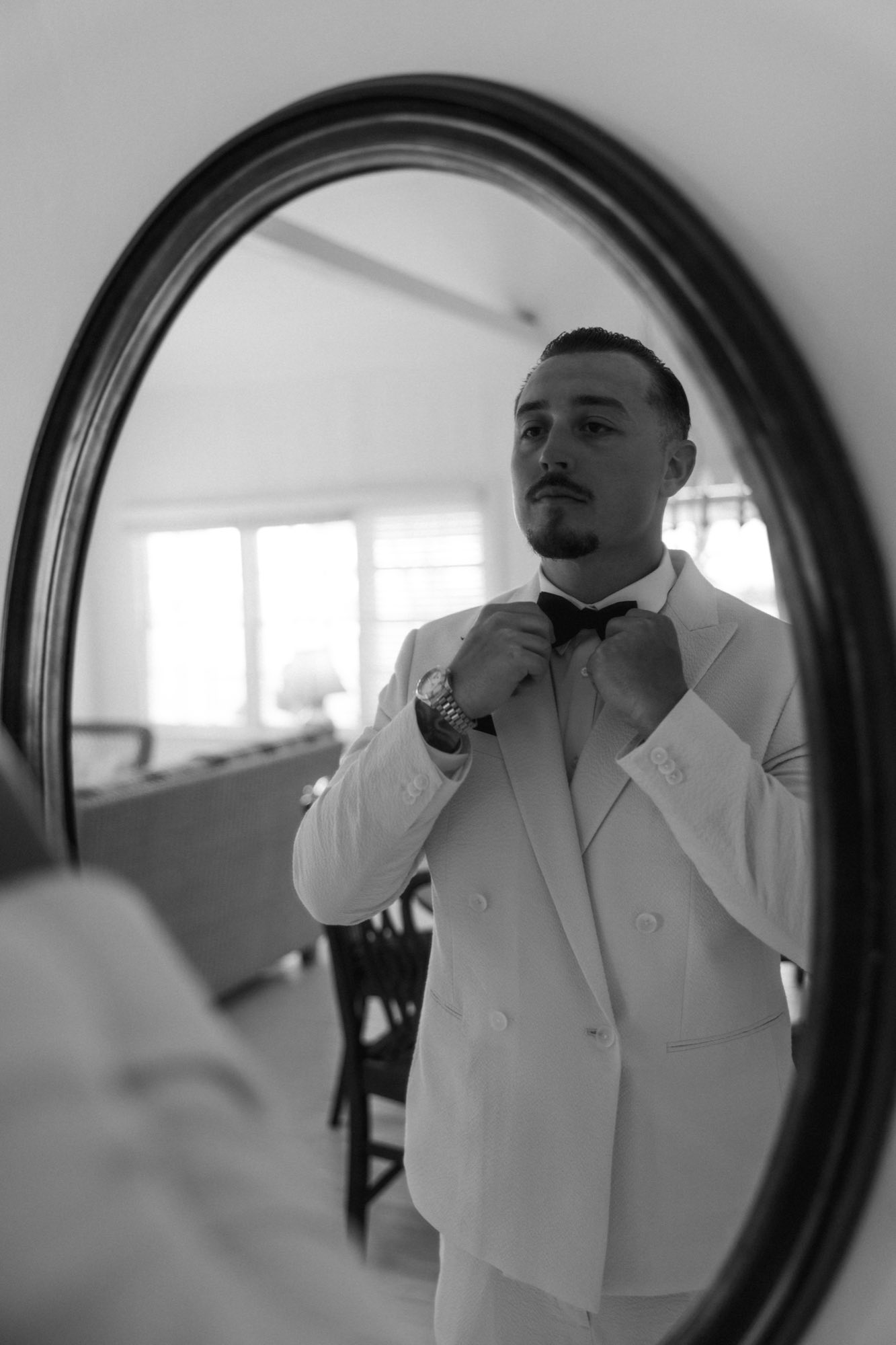 Black and white mirror reflection of groom adjusting suit during getting ready