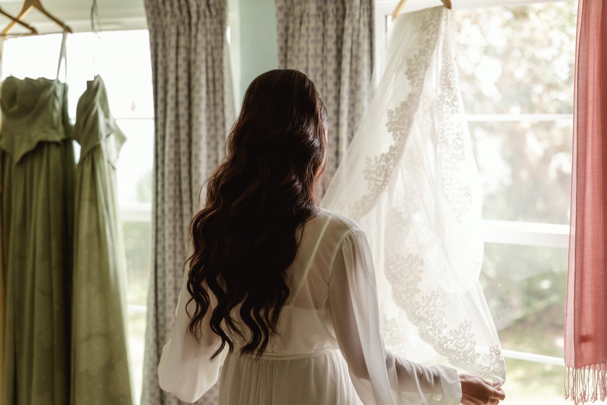 Bride admiring her lace veil by window in soft natural light during getting ready