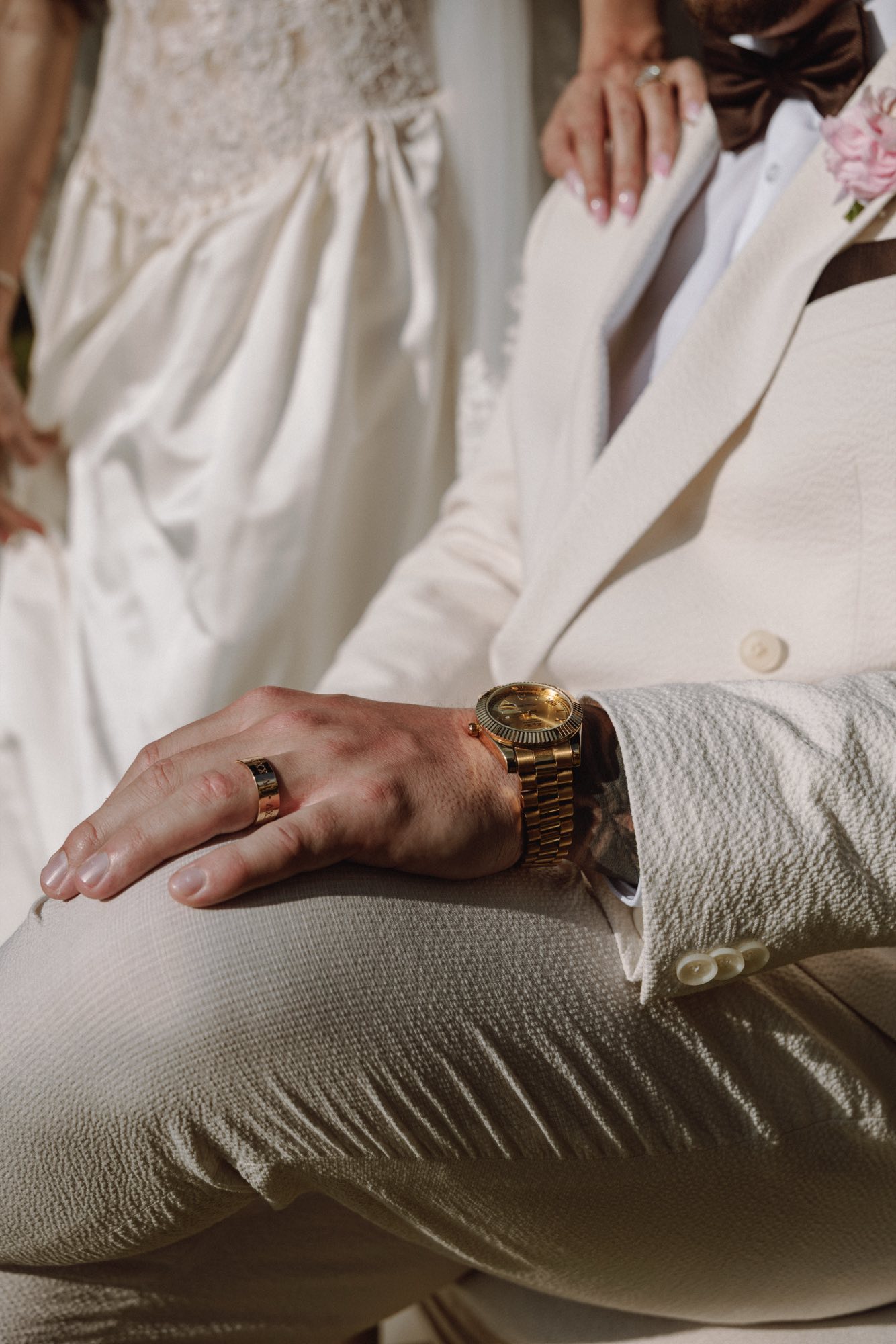 Detail of textured cream wedding suit with gold accessories