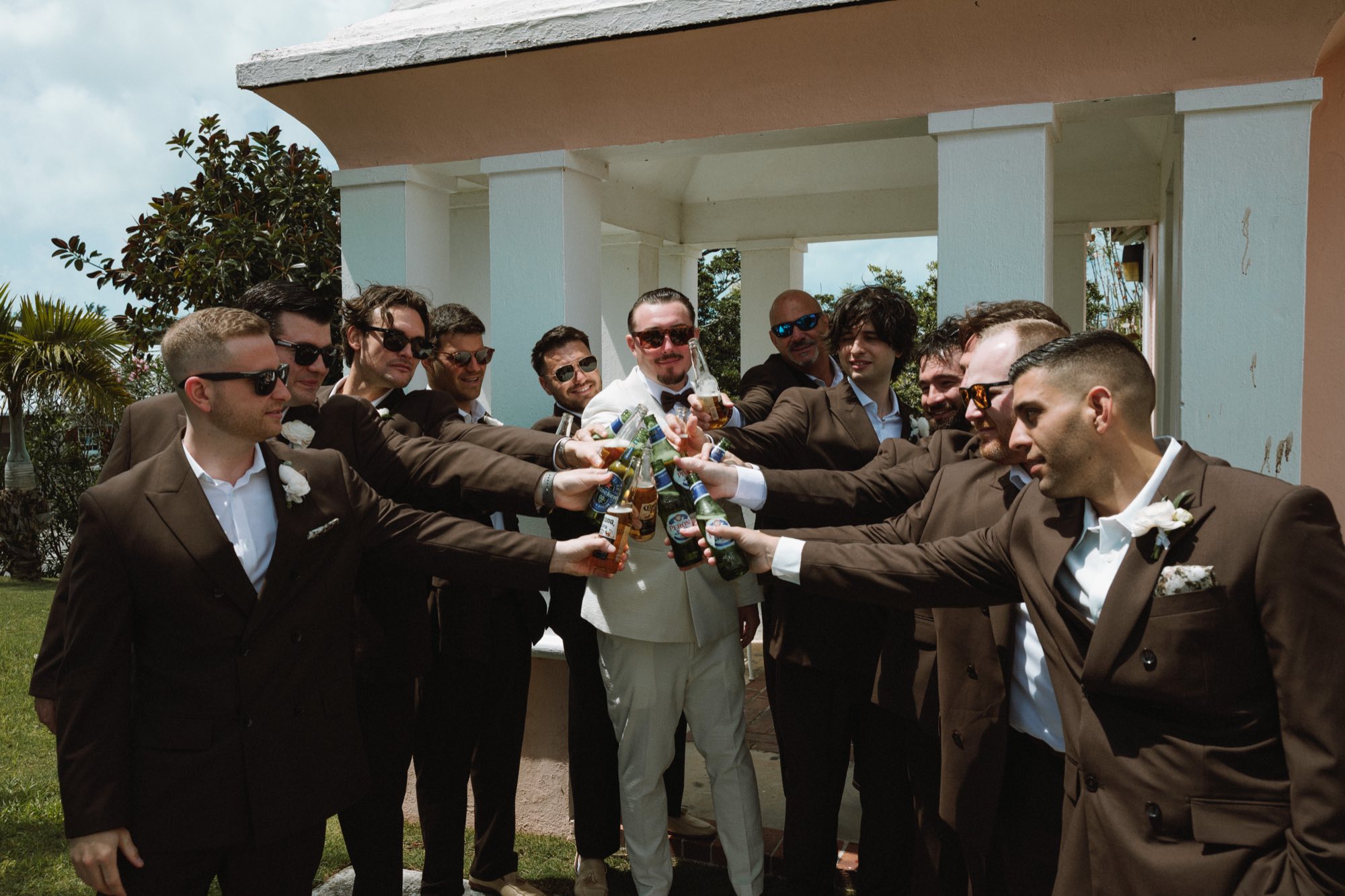 Groom and groomsmen toasting beer bottles before wedding ceremony