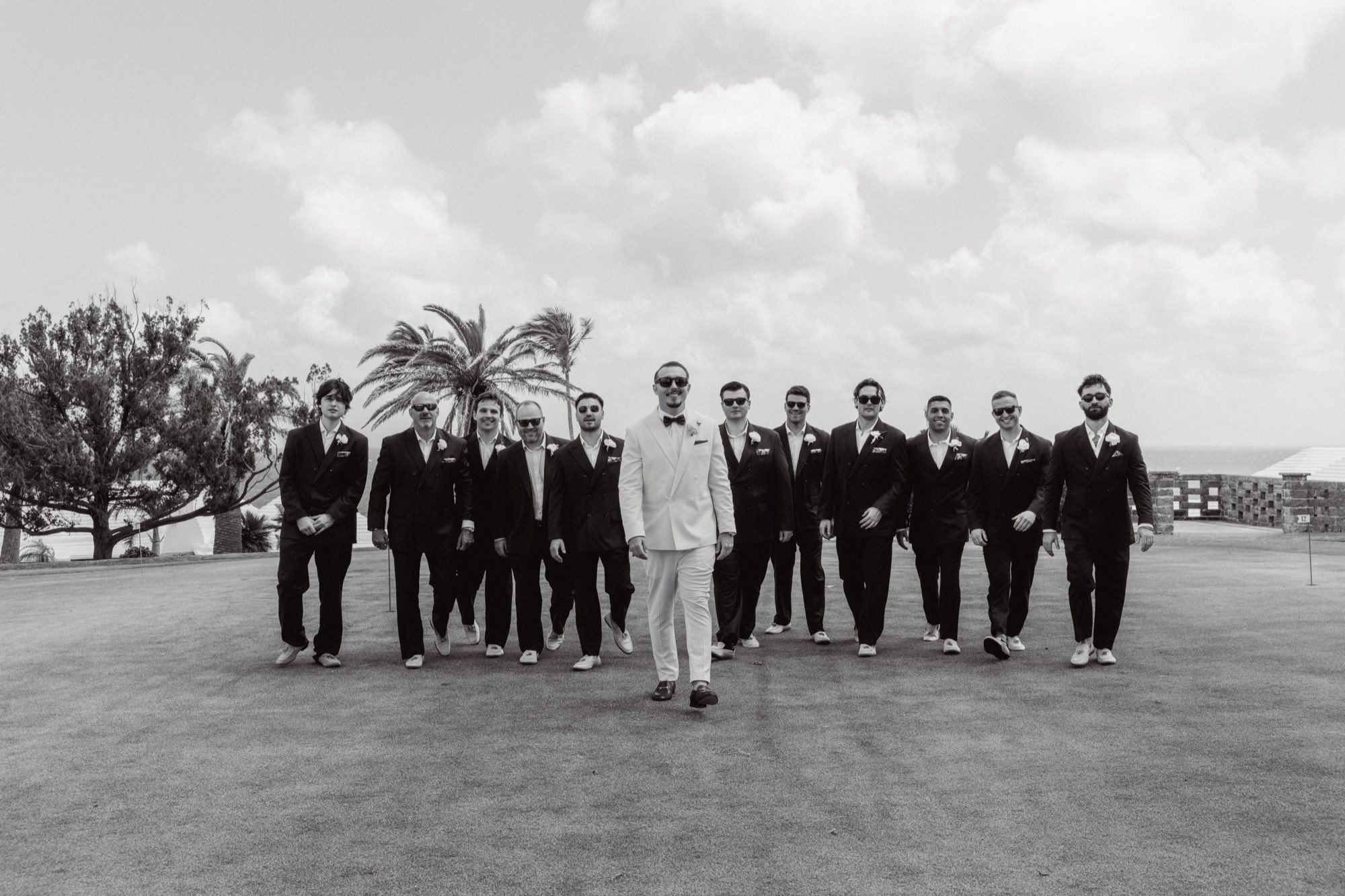 Black and white editorial shot of groomsmen walking in white suits