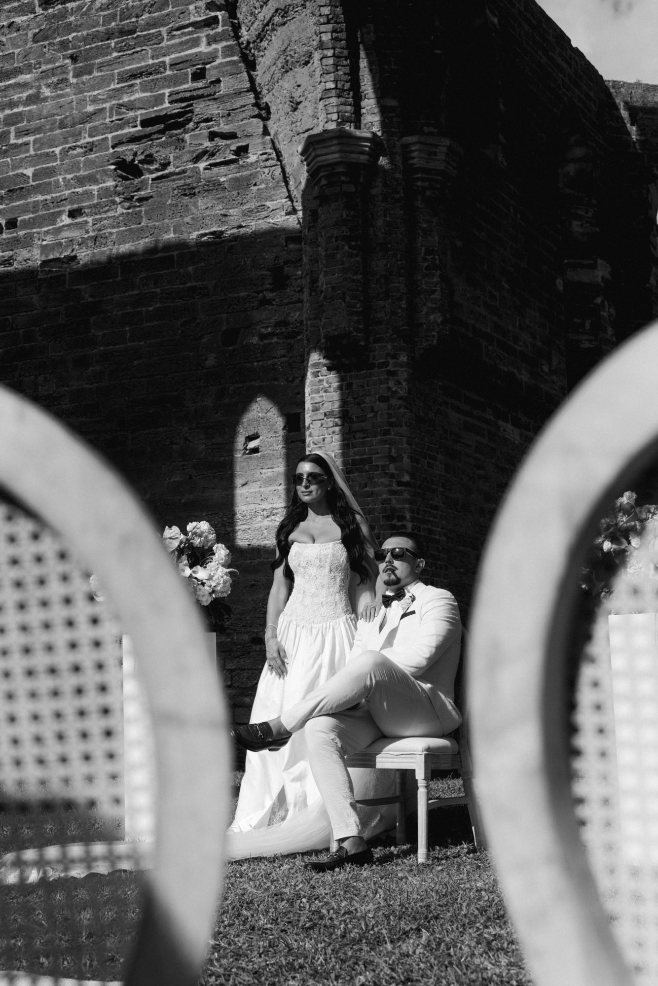 Black and white framing of couple through chair backs at outdoor ceremony