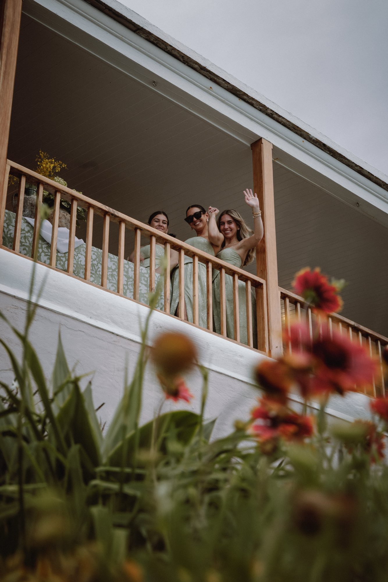 Low angle of bridesmaids waving from balcony with floral foreground