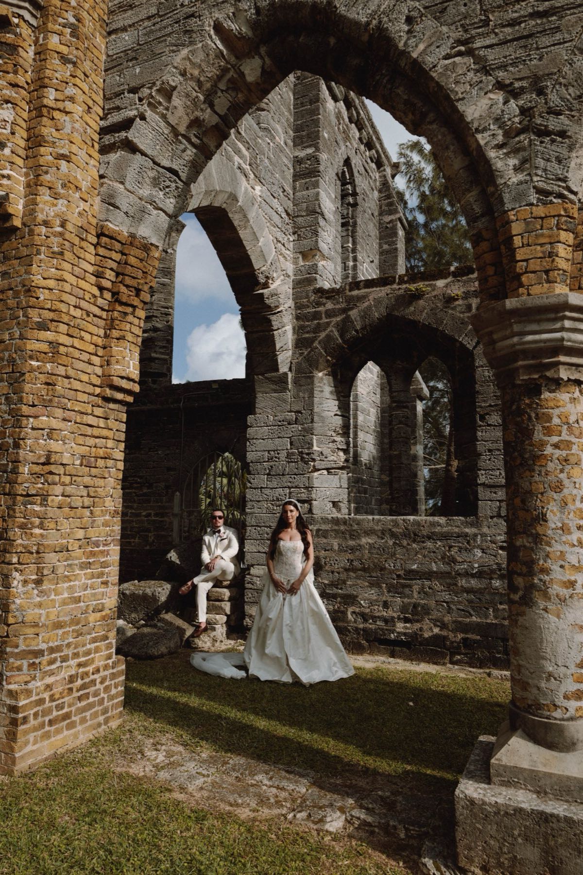 Cinematic gothic ruins frame with bride standing and groom seated on stone