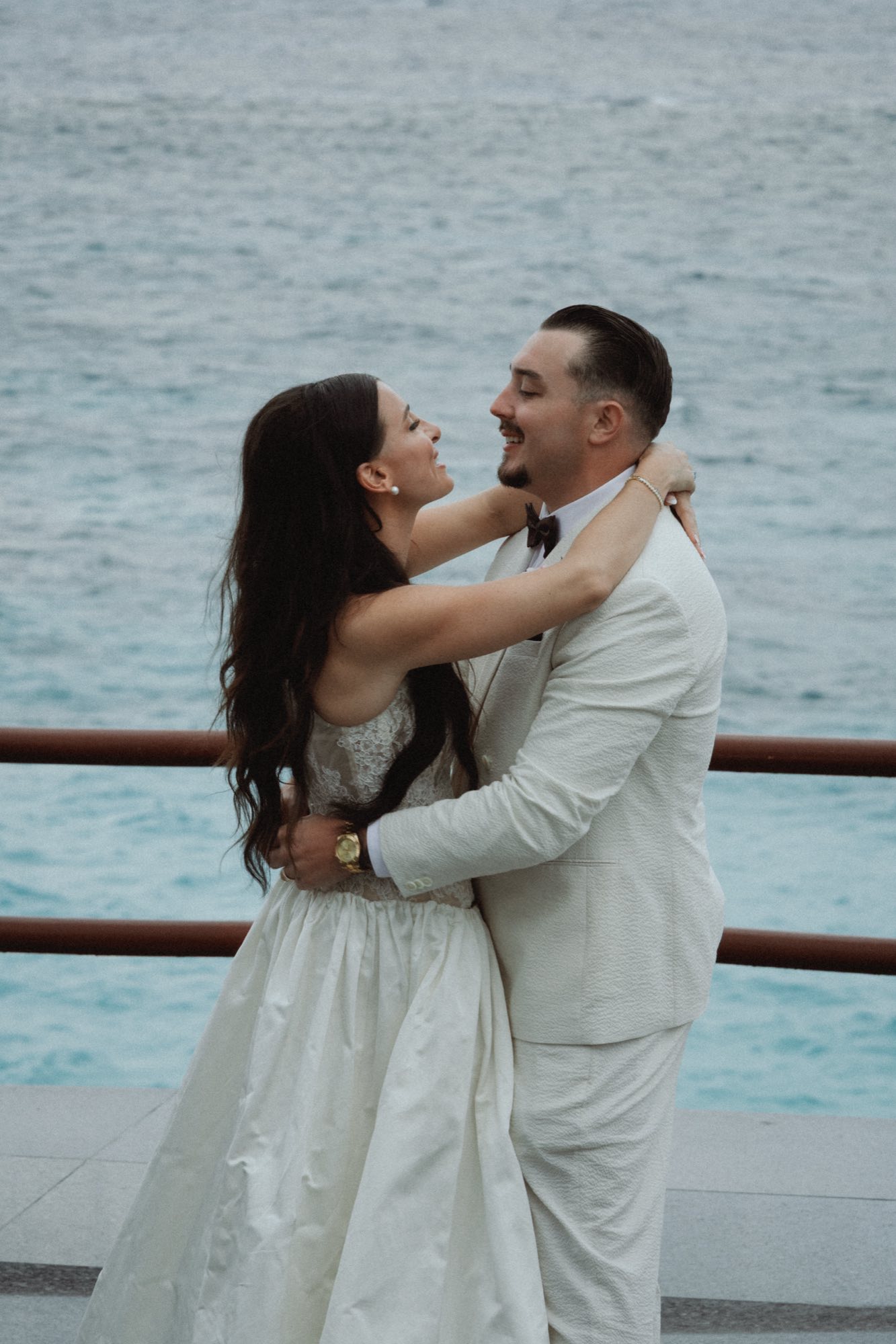 Joyful embrace between bride and groom by ocean railing at Bermuda wedding