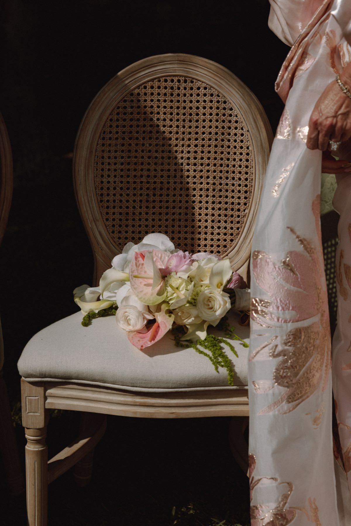 Wedding bouquet of calla lilies anthuriums and roses on cane back chair beside mother in pink jacquard at Bermuda wedding
