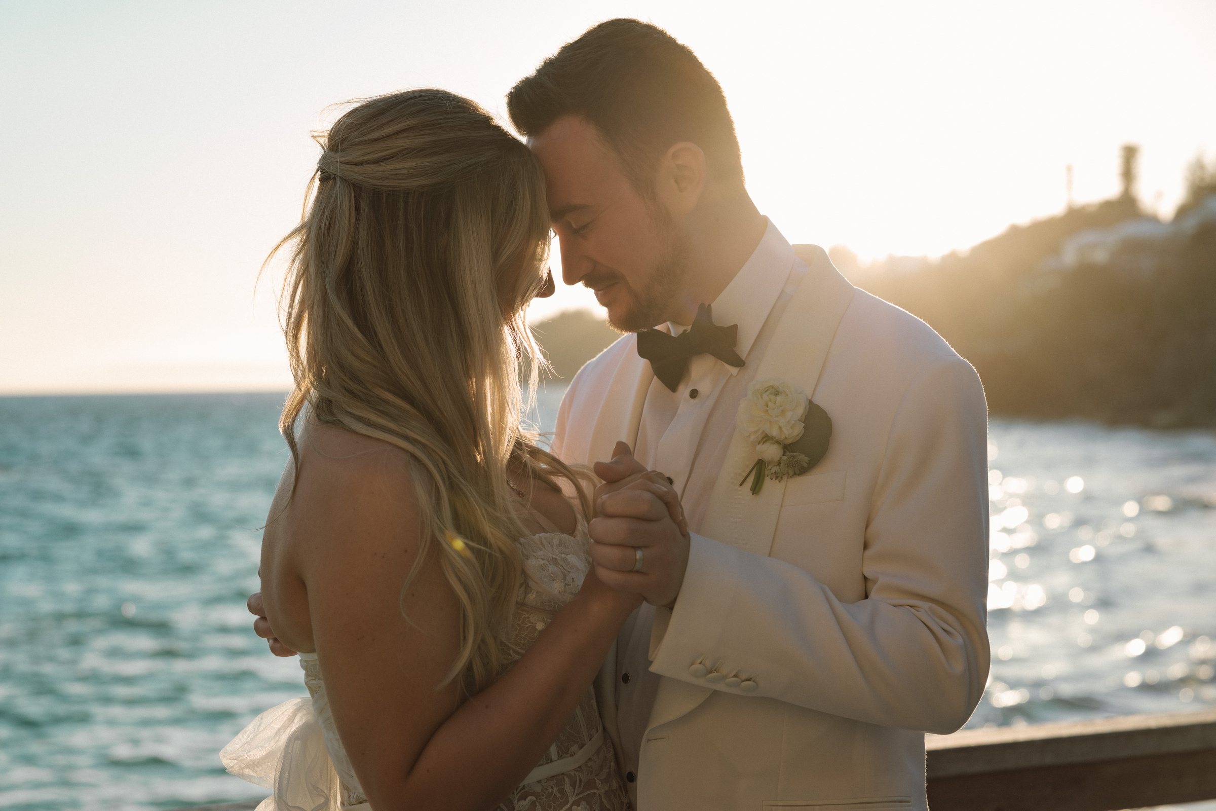 Bride and groom forehead touch at golden hour with ocean behind them at Bermuda destination wedding