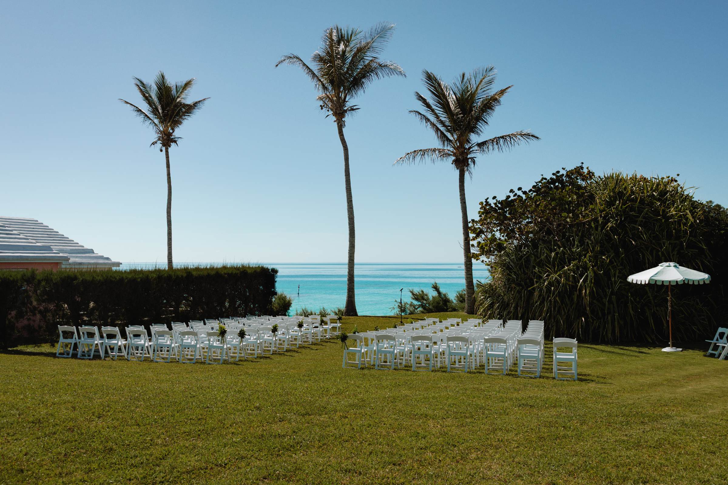 Empty ceremony chairs set on the lawn between palm trees above the Bermuda ocean