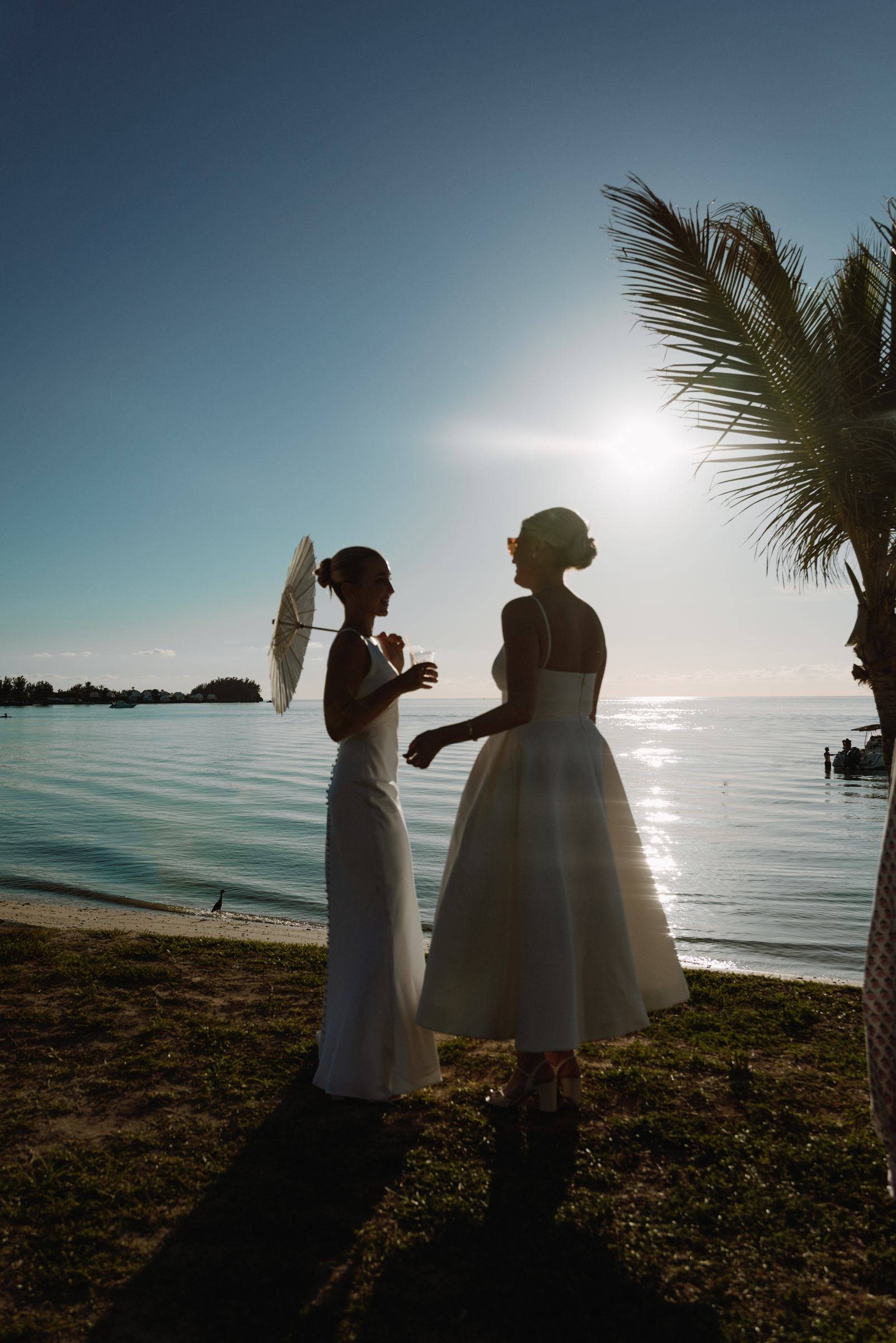 Silhouette of two brides with a paper parasol against the sun over the Bermuda water