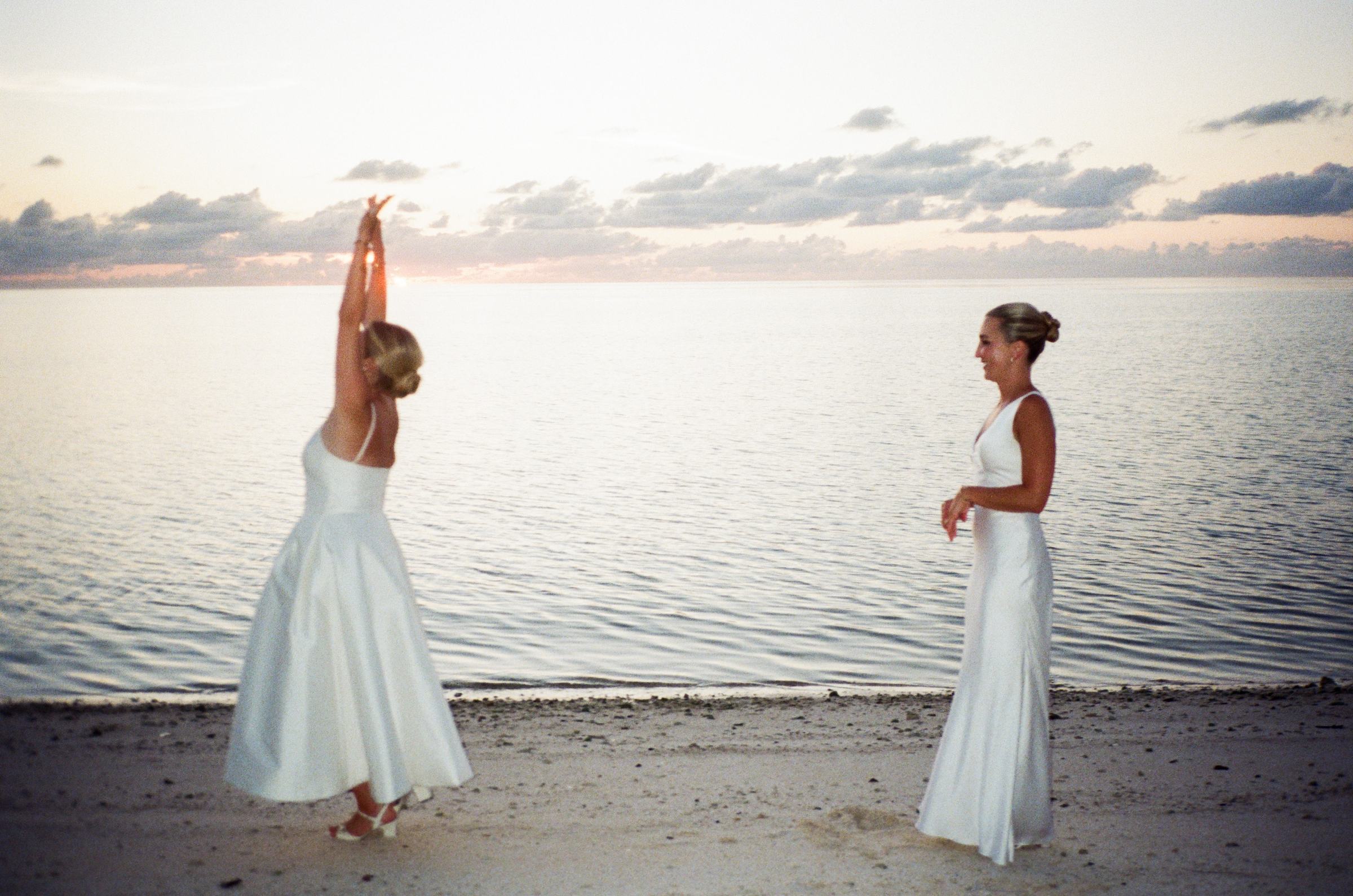 Two brides on the sand at dusk with the Bermuda water behind them
