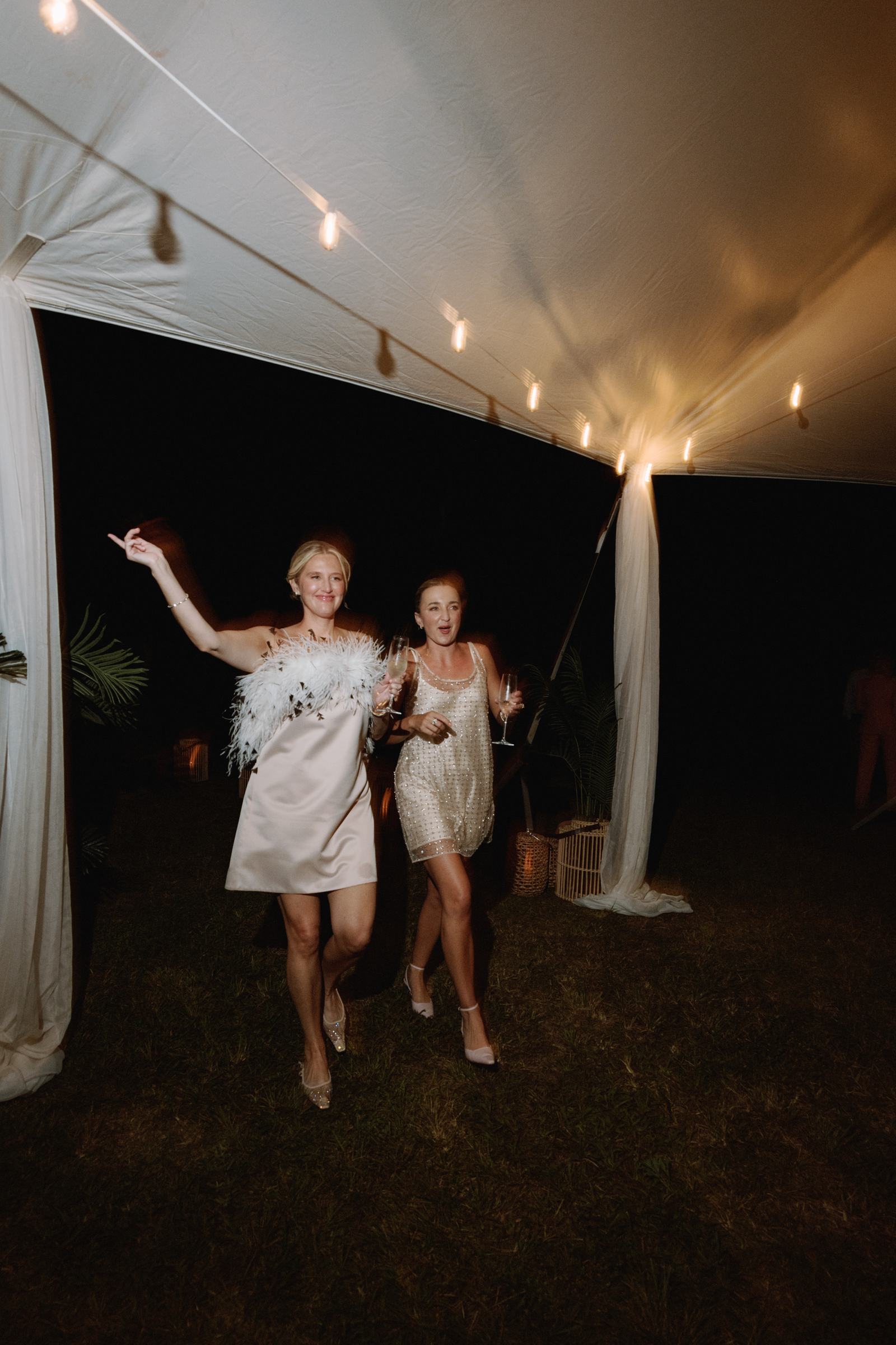 Two brides running through the tent at night during their wedding reception