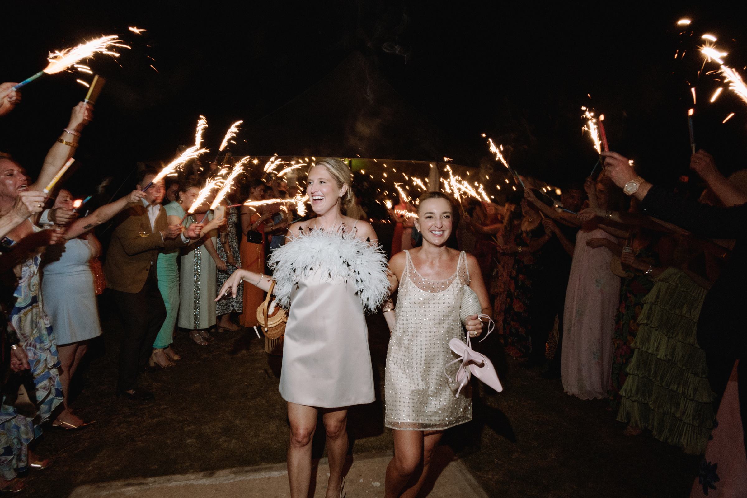 Two brides laughing as they run through a sparkler exit at their Bermuda wedding