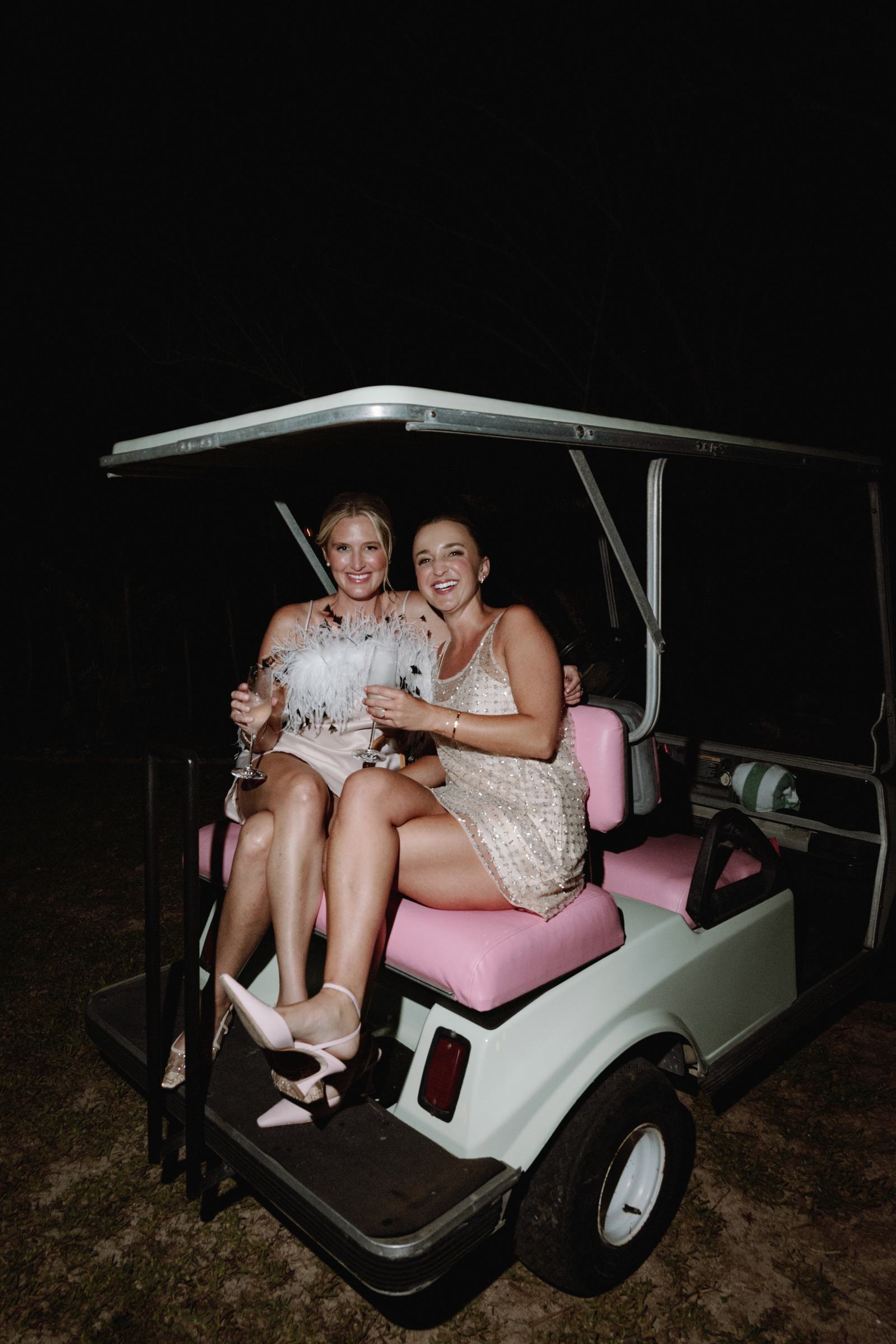 Two brides on a golf cart lit by flash at night after their Bermuda wedding