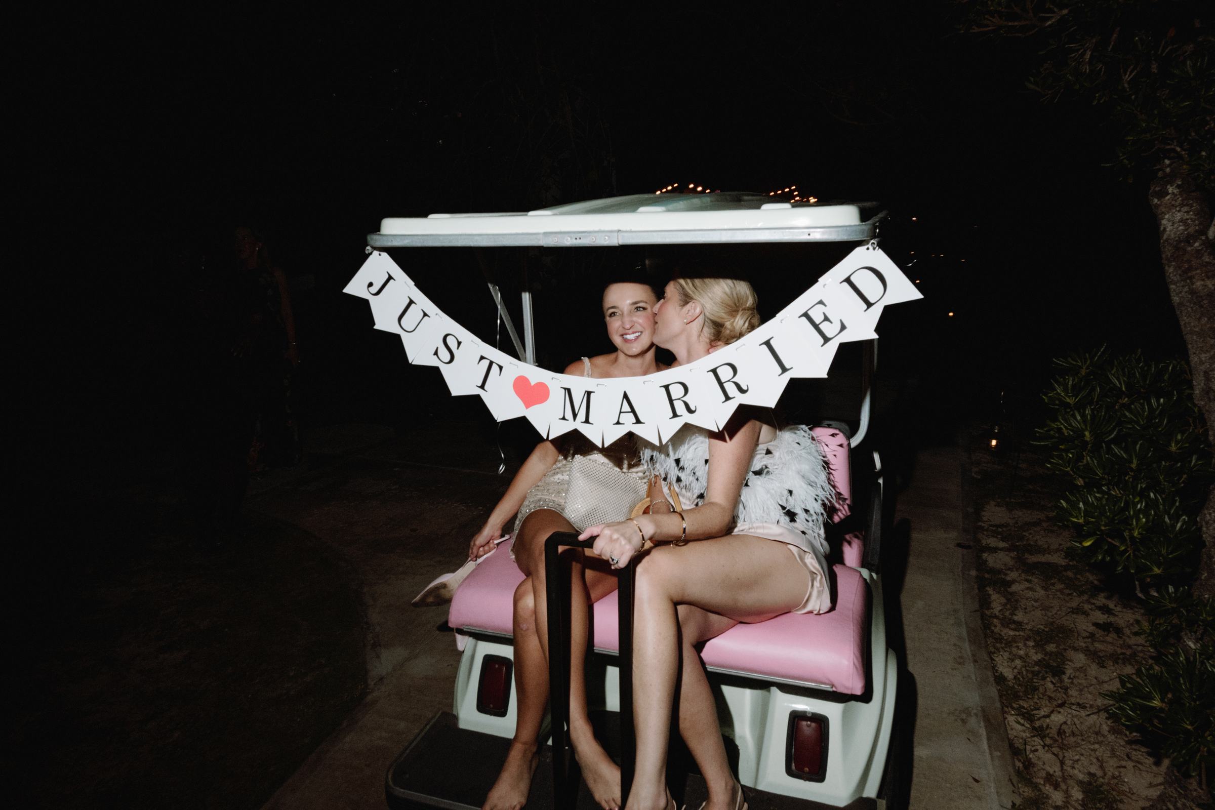 Two brides on a golf cart with a just married banner after their Bermuda wedding