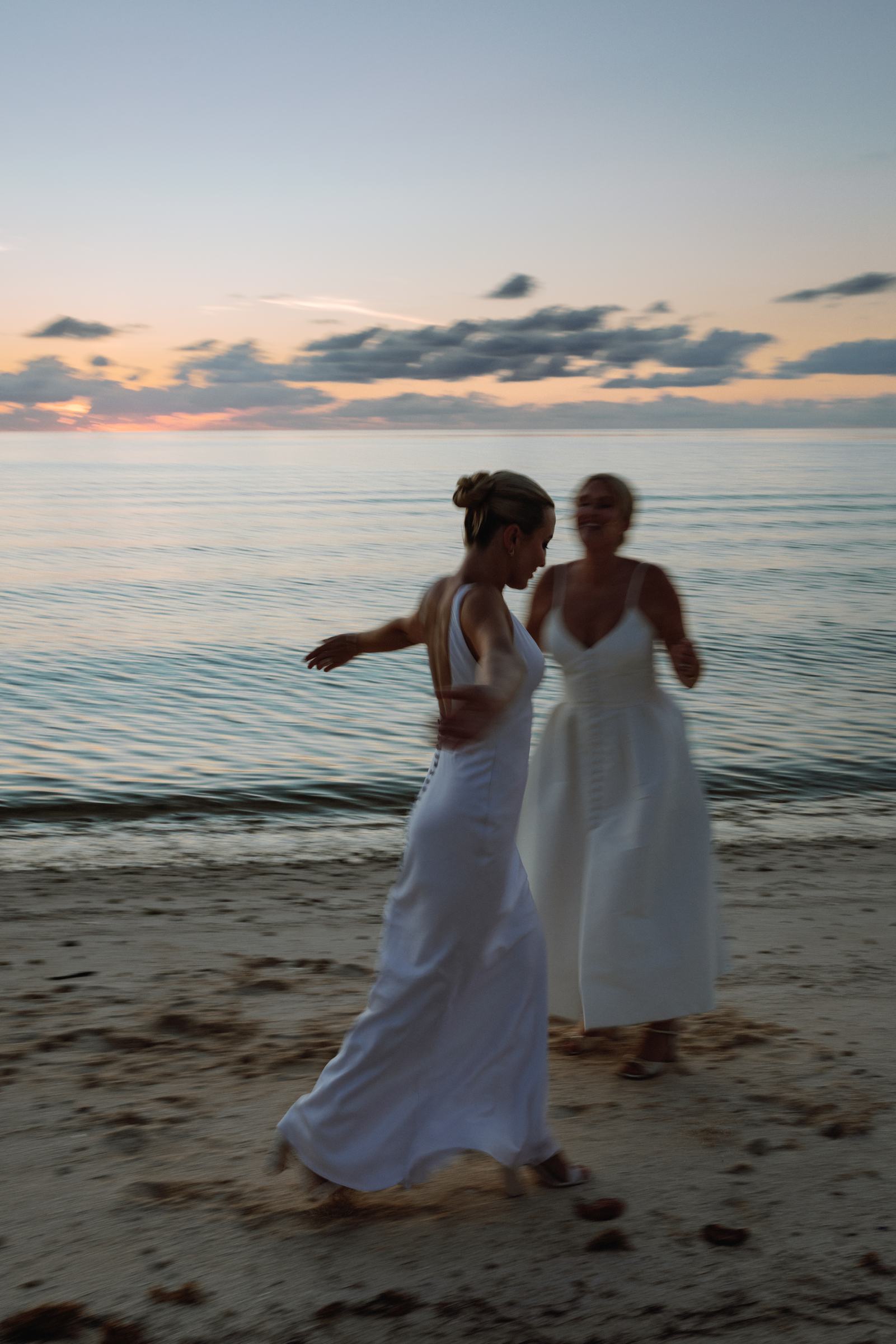 Two brides walking barefoot along the beach at dusk in Bermuda