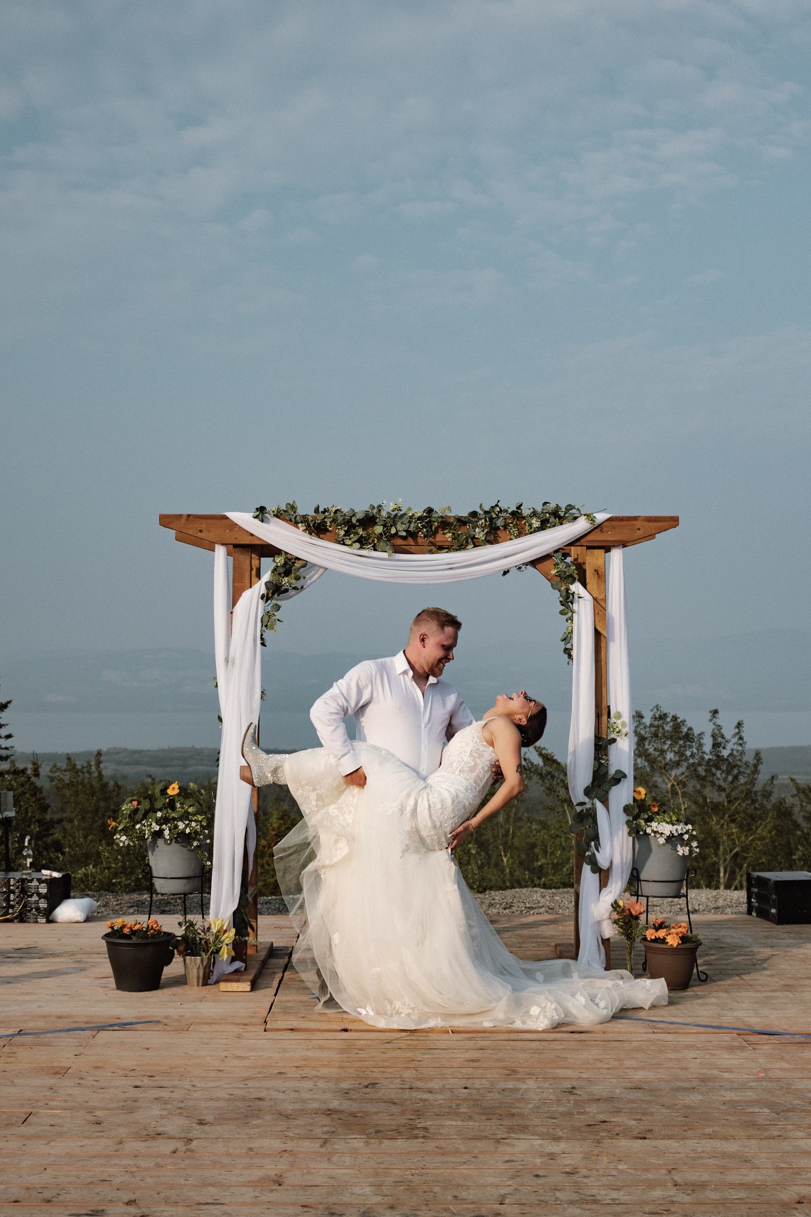 Bride and groom dip kiss beneath the ceremony arch on a mountaintop deck