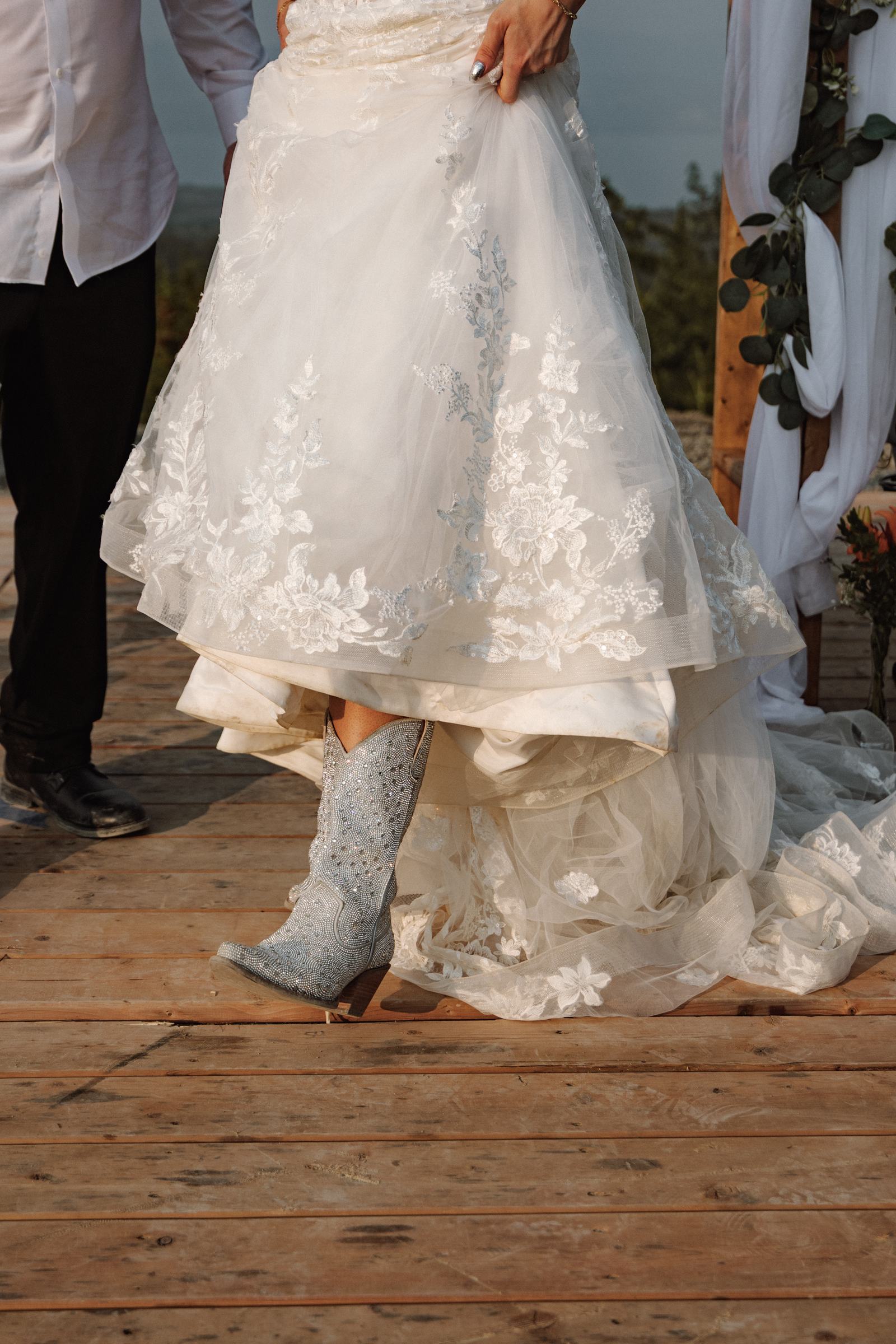 Cowboy boots under a lace wedding dress on the wooden reception deck