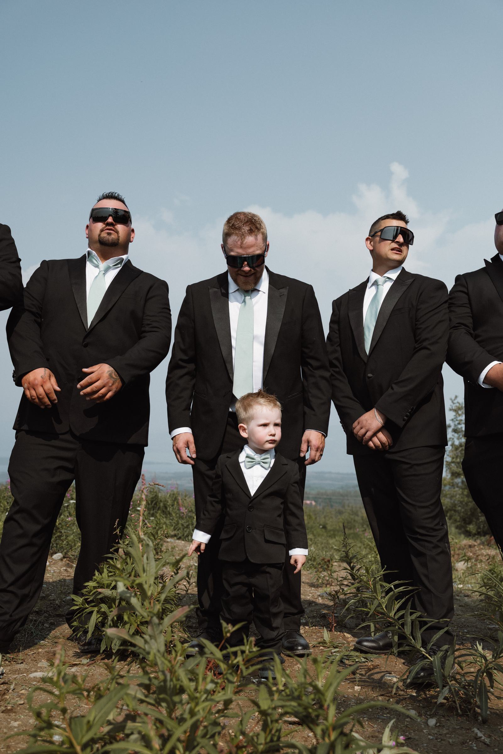Groomsmen in black suits with the young ring bearer among them