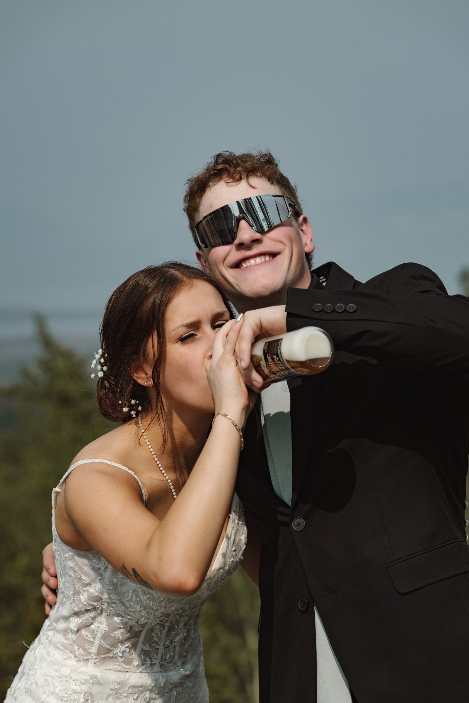 Bride and groom laughing with a bottle of champagne in sunglasses