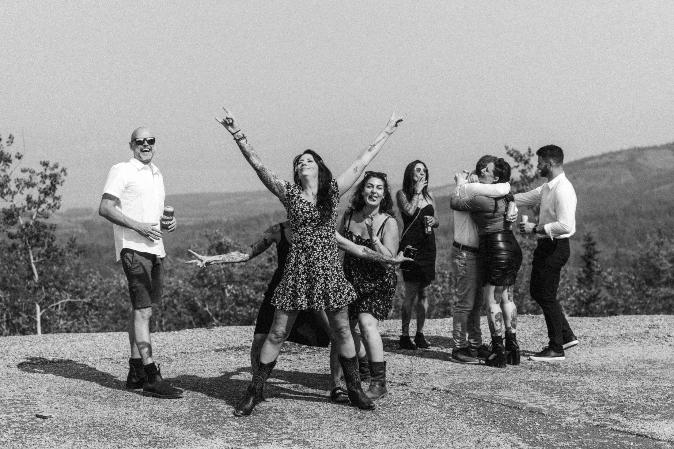 Black and white photograph of the whole wedding party jumping on a gravel road
