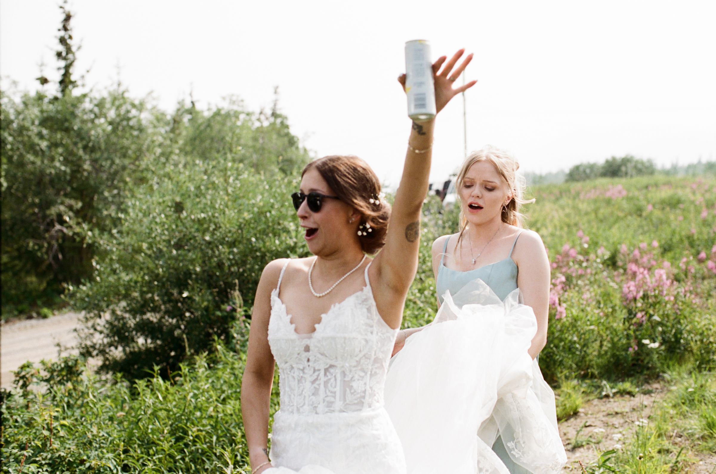 Two guests raising a beer as they walk through the fireweed, shot on film