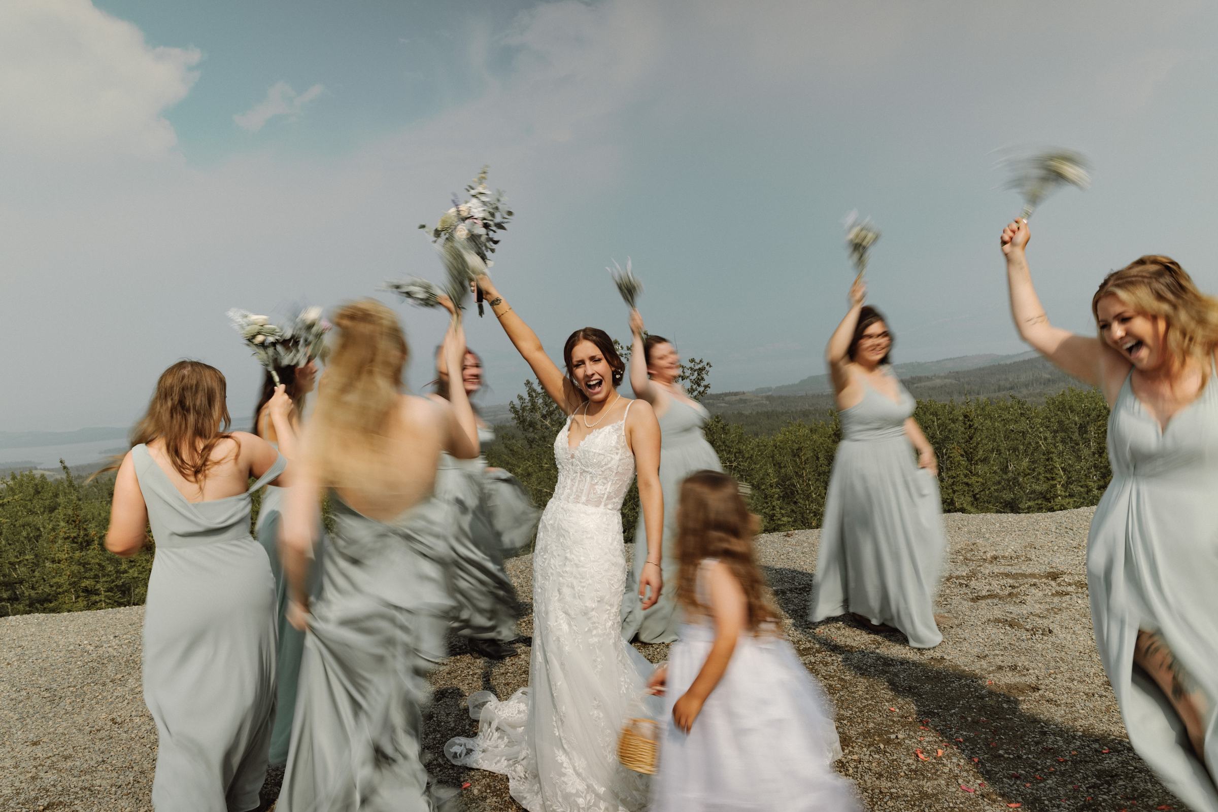 Bridal party cheering with bouquets flying at a mountaintop wedding