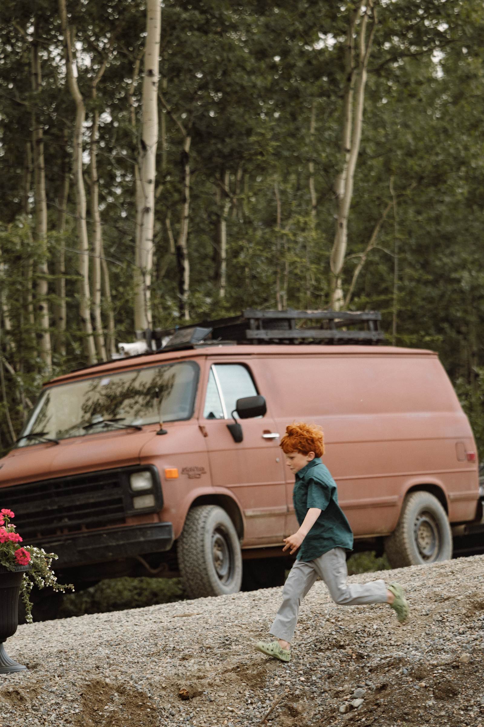 Child running past the vintage brown van at a wedding in the woods