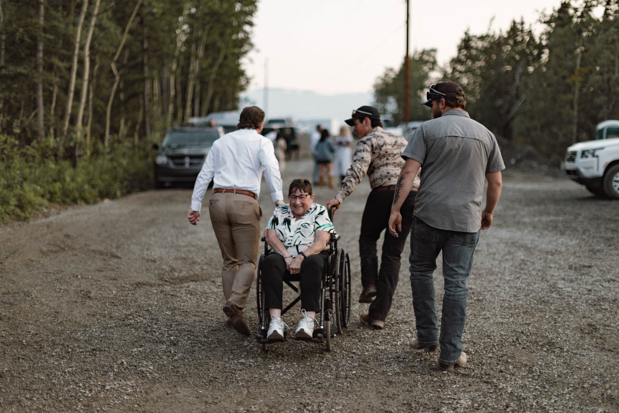 Guests pushing a friend in a wheelchair up the road to the reception