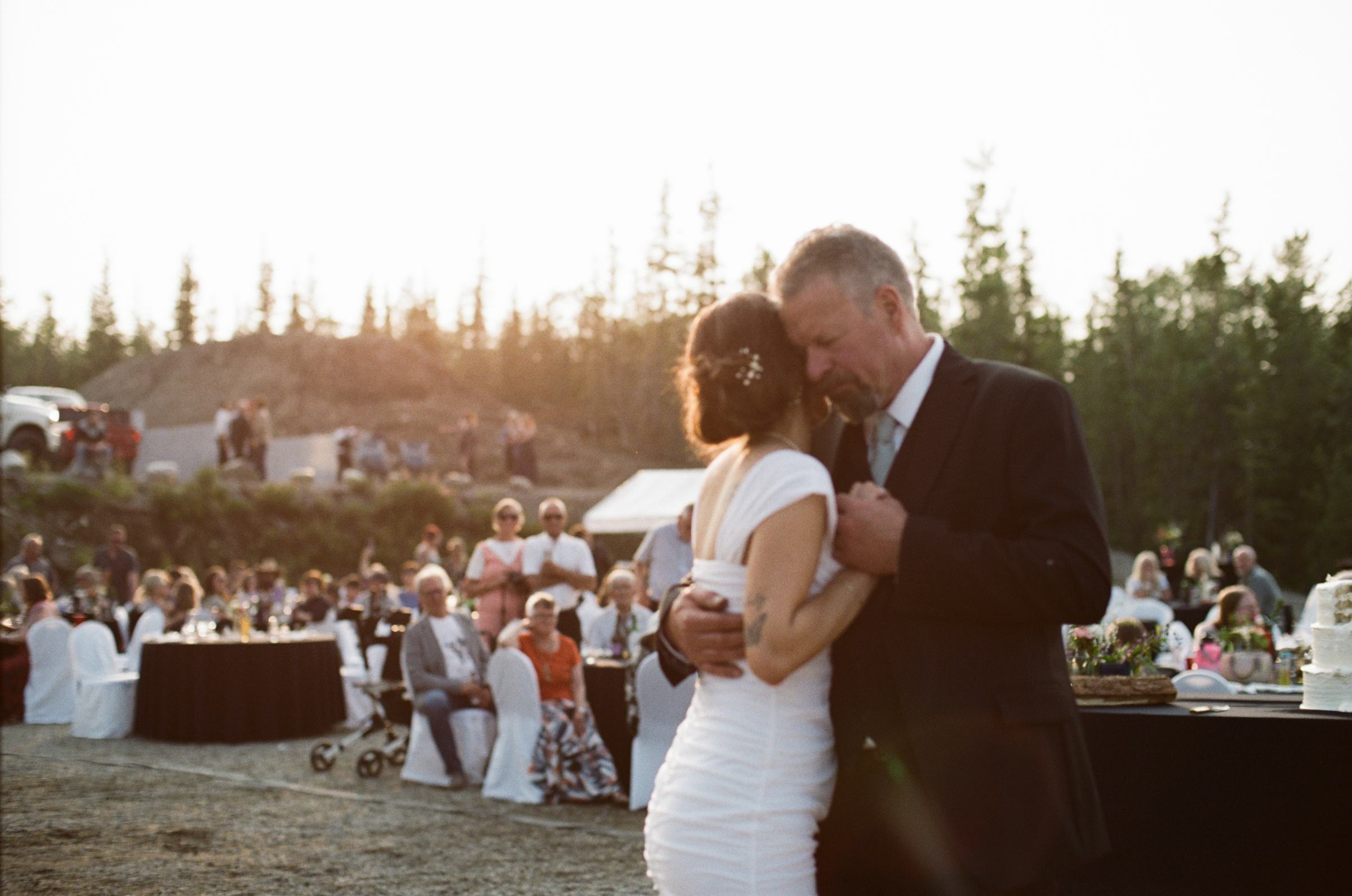 Father and daughter dance at golden hour with the wedding guests behind them