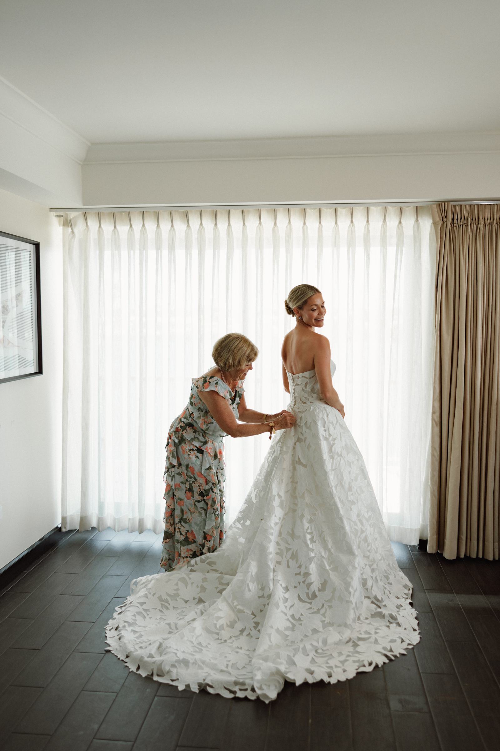 Bride being helped into her gown by her mother in soft window light