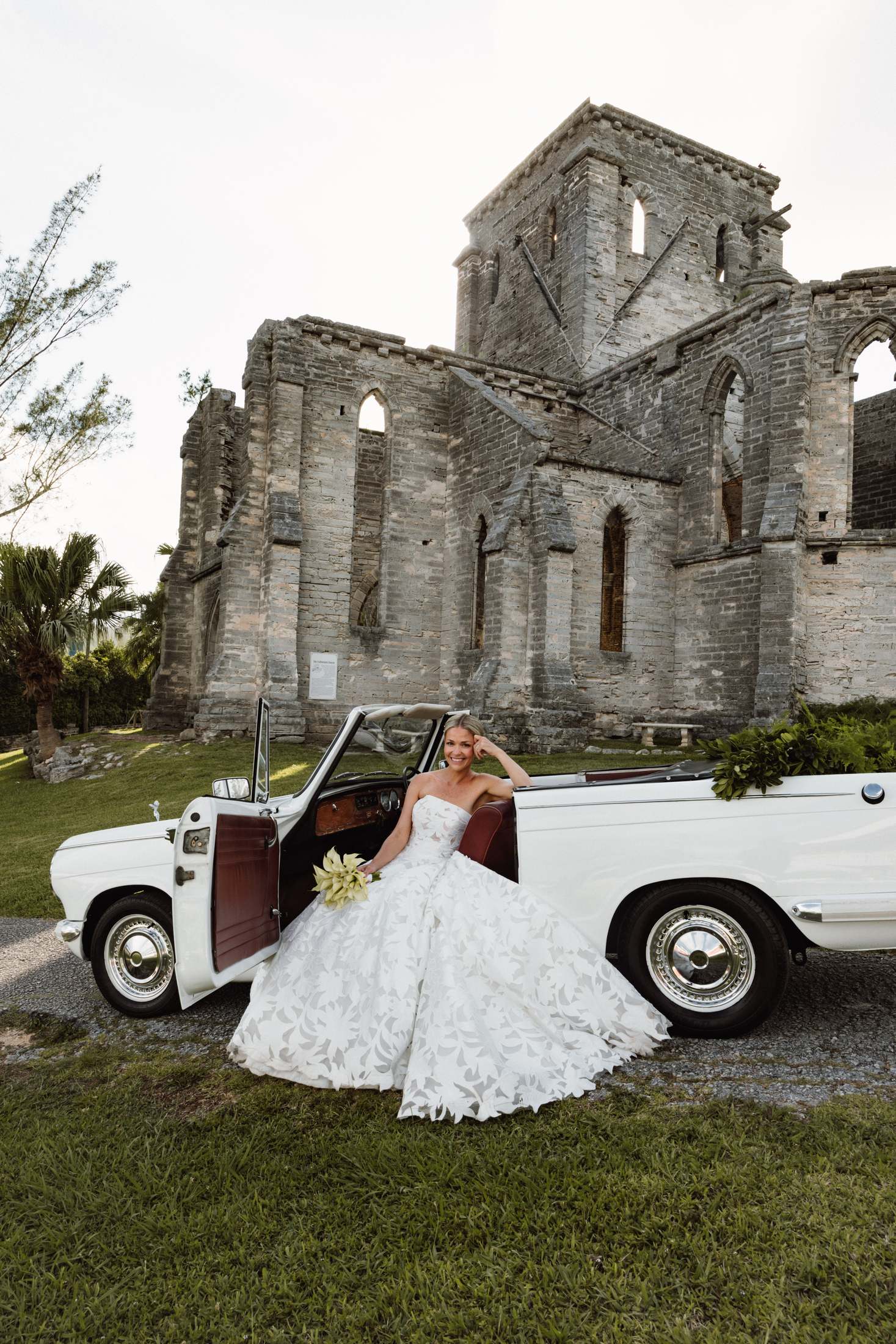Bride seated on a white vintage convertible in front of the Bermuda church ruins