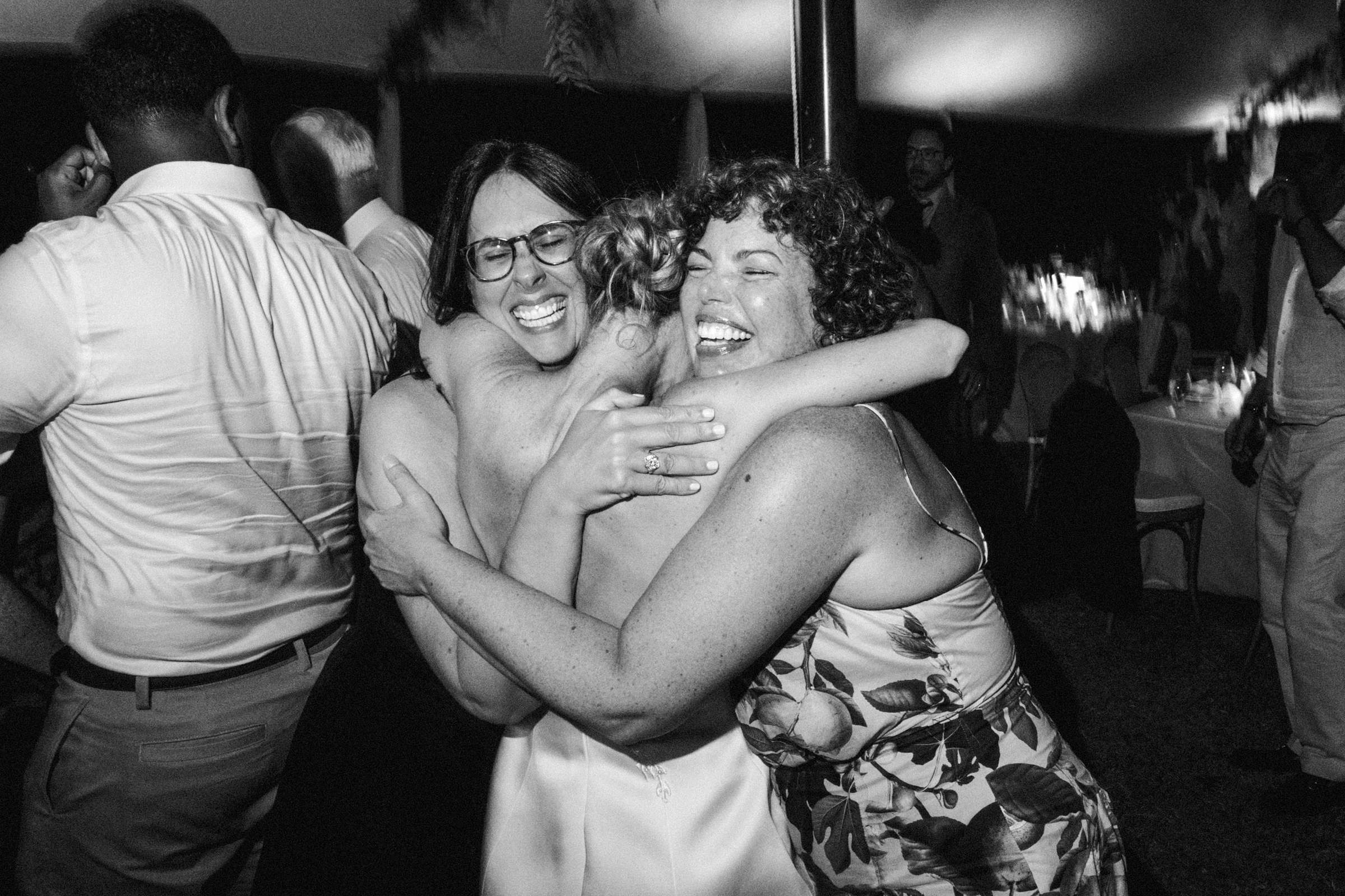 Black and white photograph of guests hugging and laughing on the dance floor