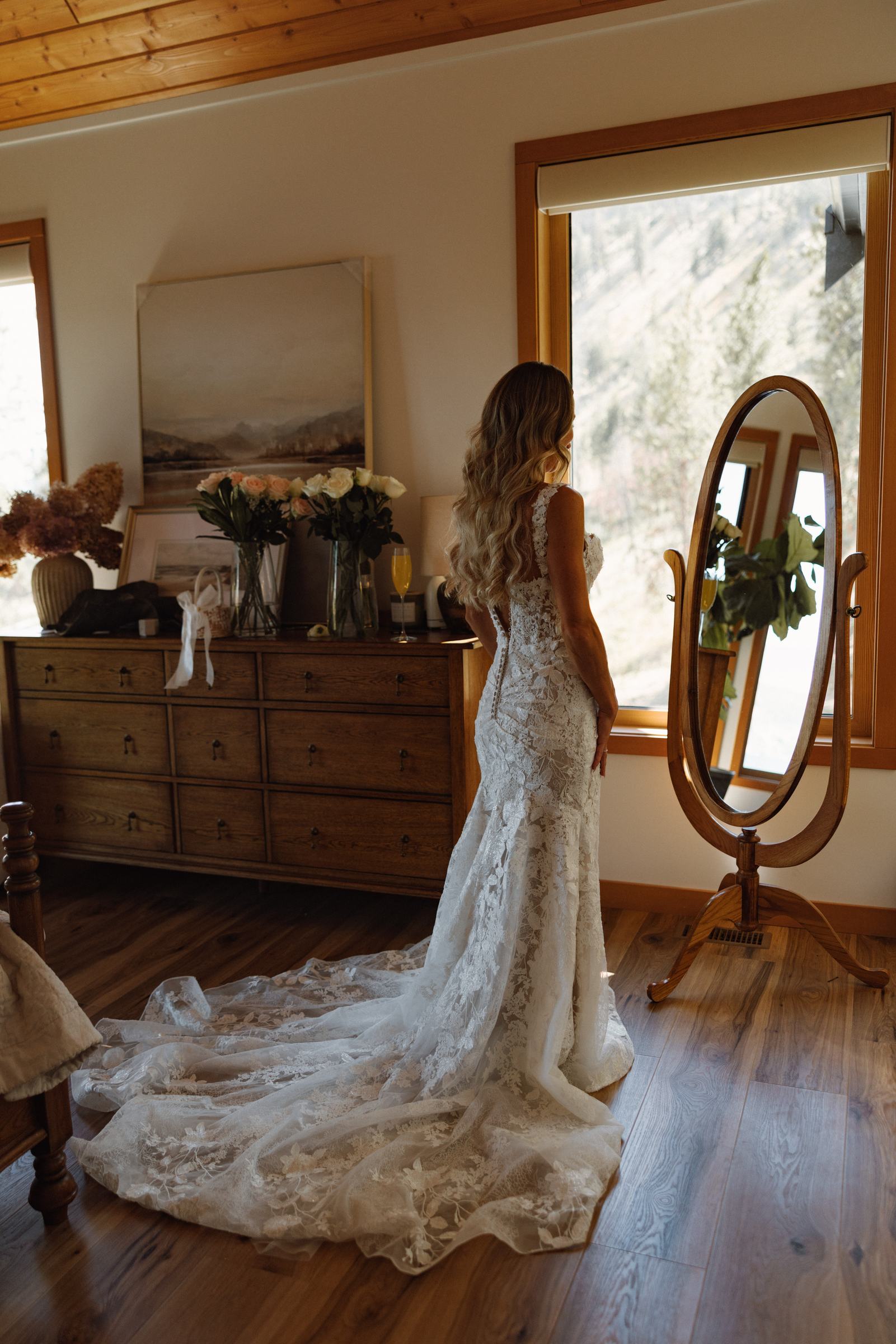 Bride alone in the room beside a standing mirror in her lace gown