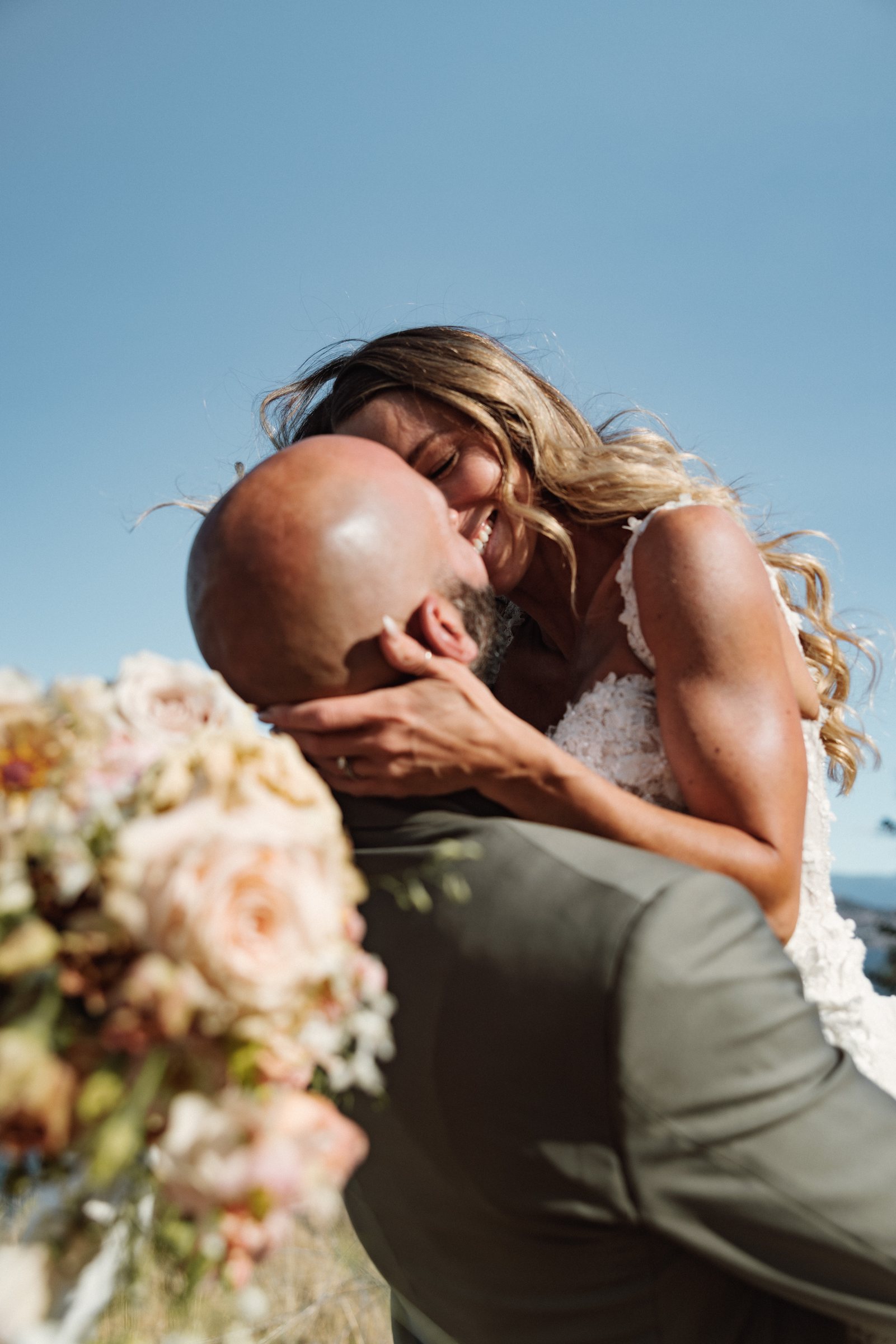 Bride and groom kissing with her hands on his face and the bouquet raised