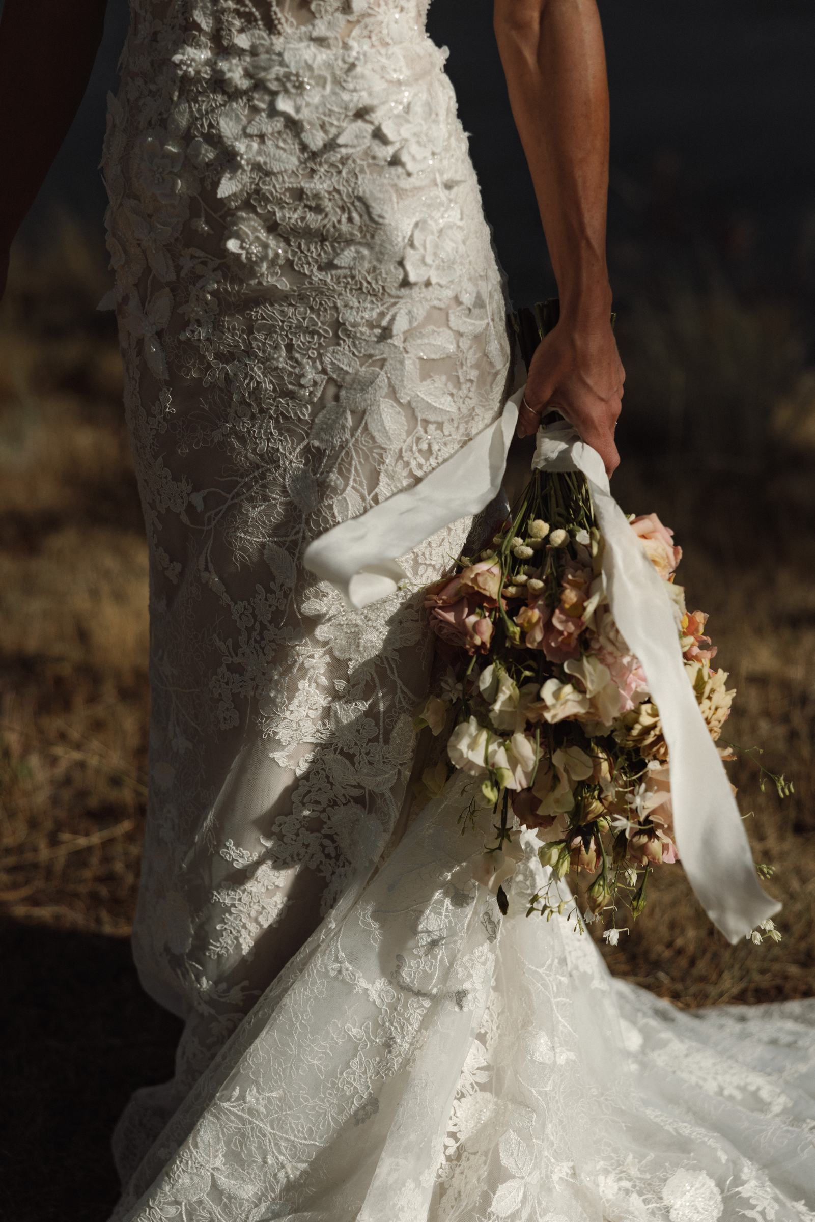 Bouquet held at the bride's side against the texture of her lace gown