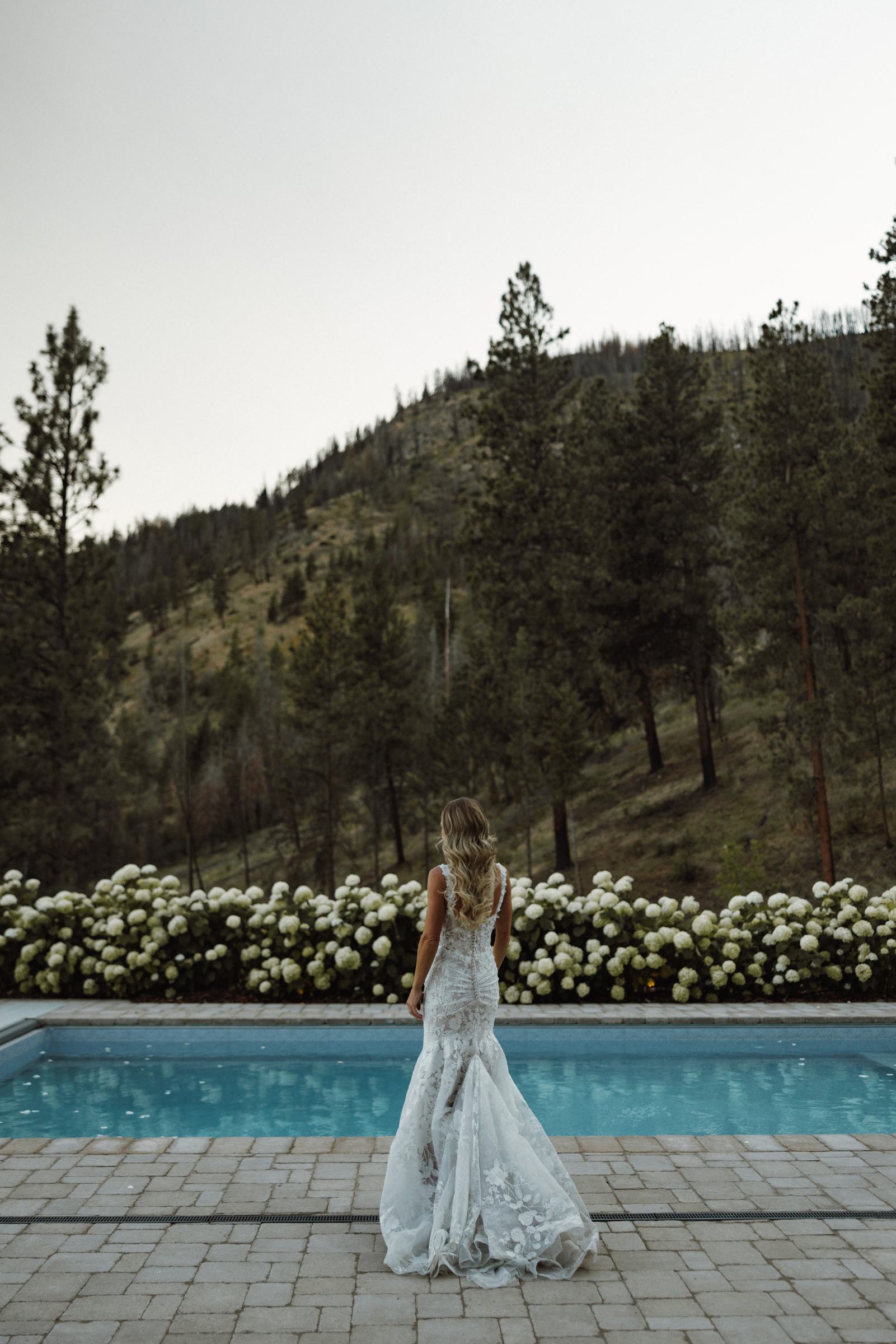 Bride walking beside the pool in her gown with the hills behind her