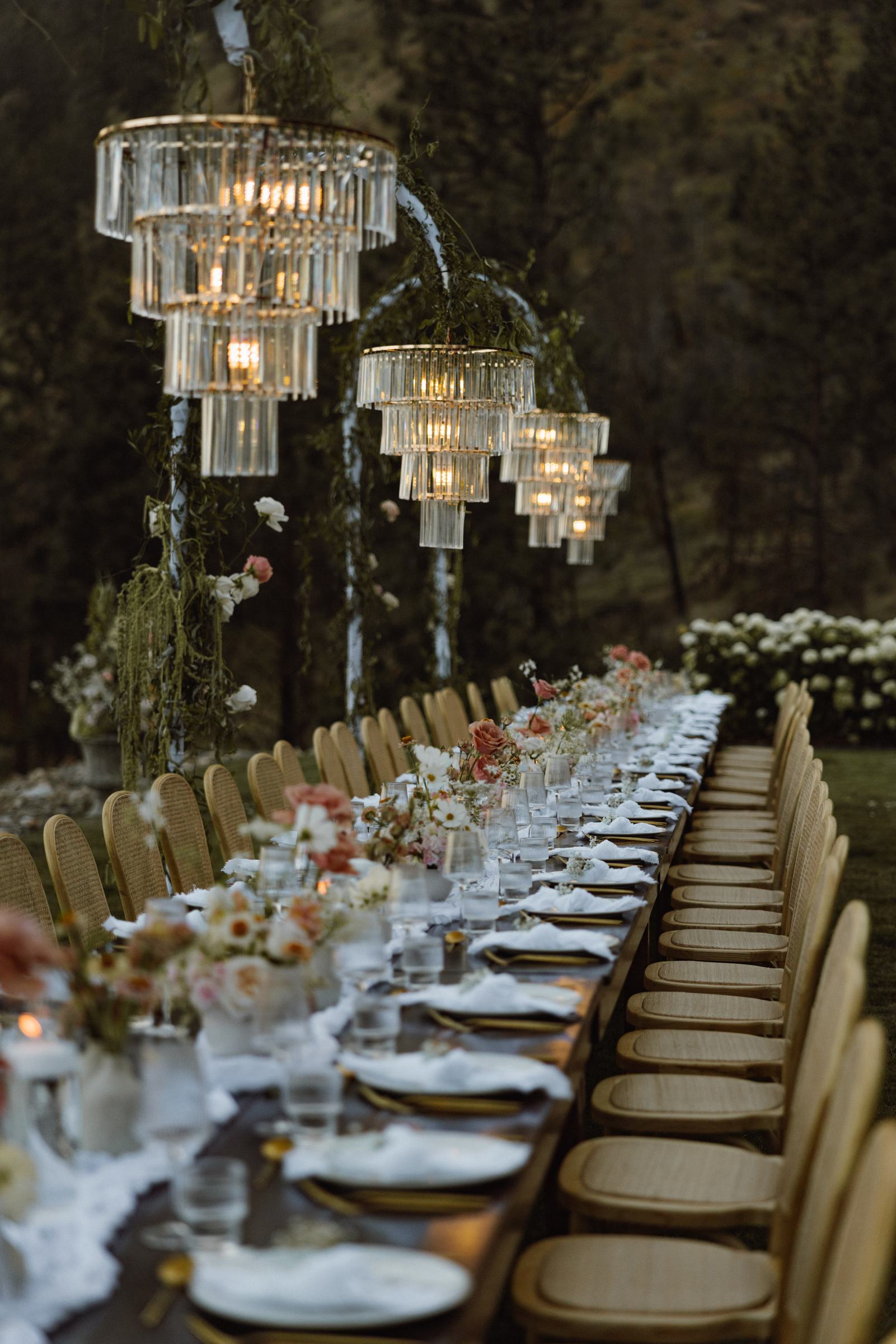 Long reception table beneath crystal chandeliers hung in the trees