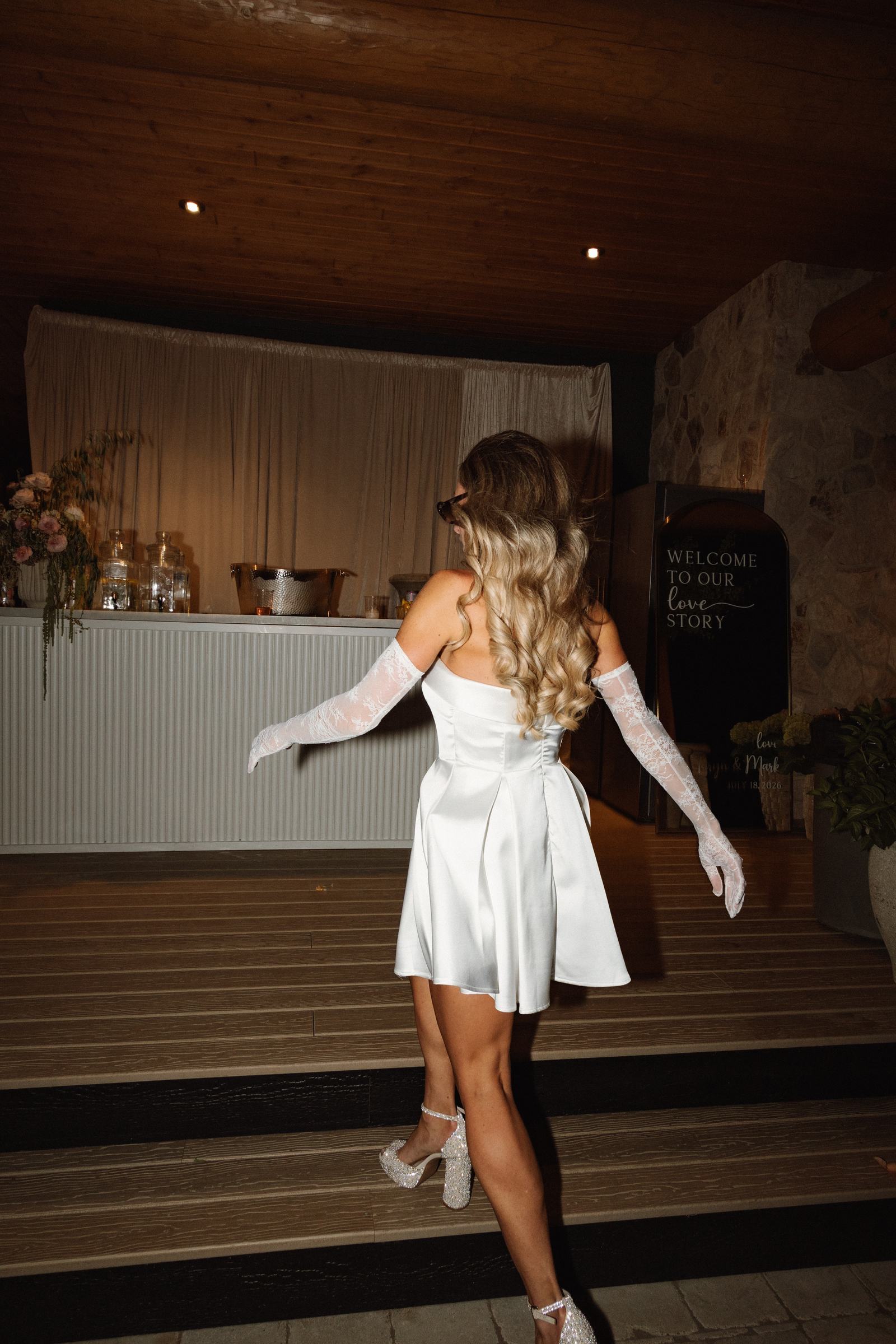 Bride in her short reception dress with her arms out in warm light